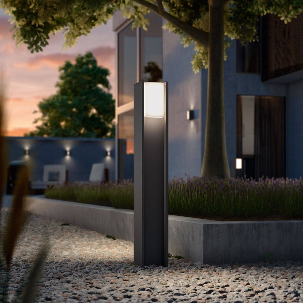 Ciemny słup oświetleniowy stoi na kamienistej ścieżce przed nowoczesnym domem.