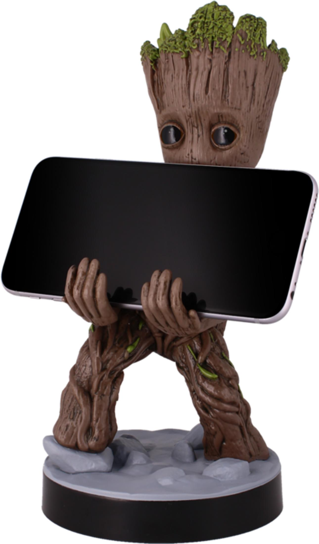 Baby Groot tiene uno smartphone nero con entrambe le mani su una base rocciosa.