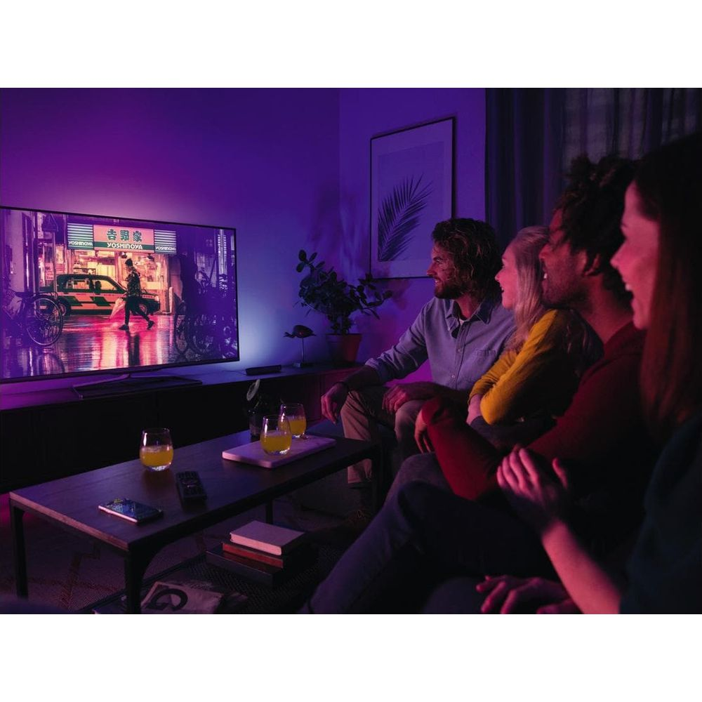 Quatre amis assis sur un canapé regardent la télévision. La pièce est éclairée en violet.