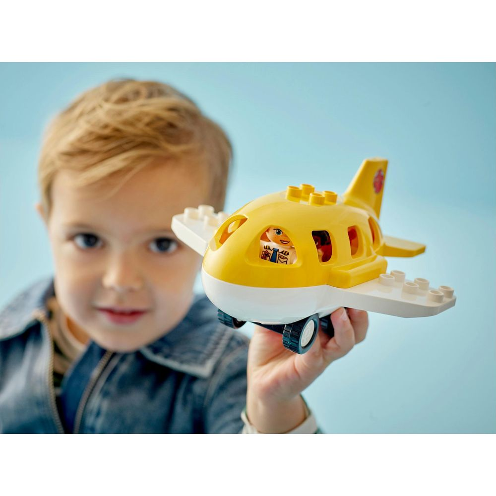 Chłopiec trzyma żółty samolot-zabawkę z białymi skrzydłami i figurkami.