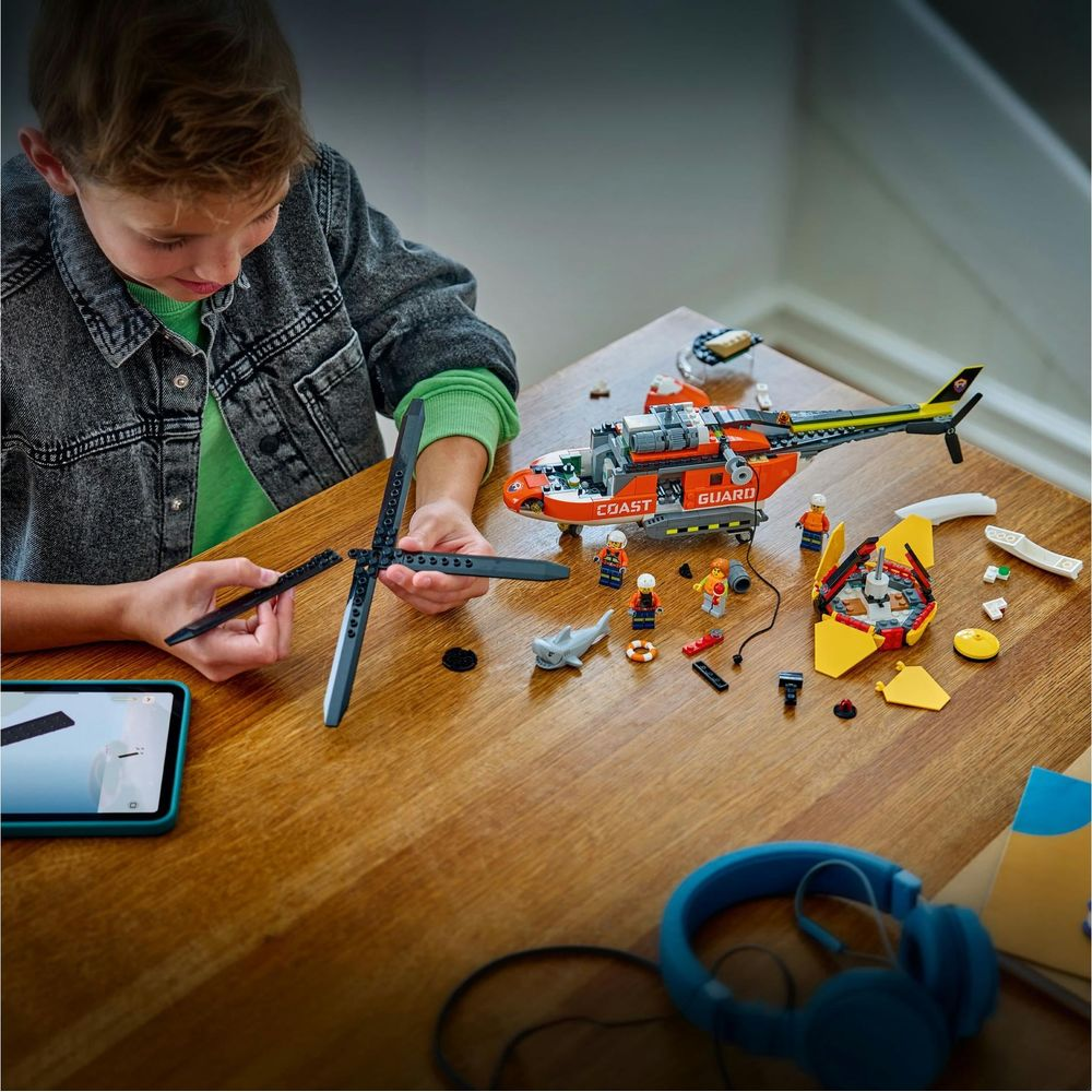 Dziecko buduje helikopter Lego na drewnianym stole, rozłożone części i instrukcje.