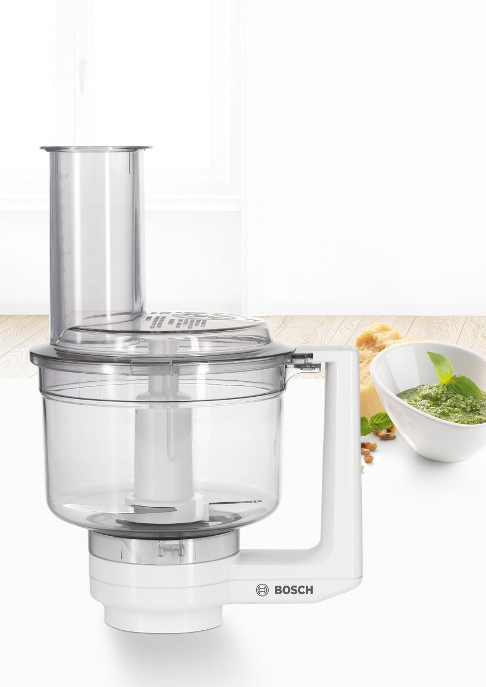 Ein weißer Bosch Küchenmaschinen-Aufsatz mit transparentem Behälter und Pesto daneben.