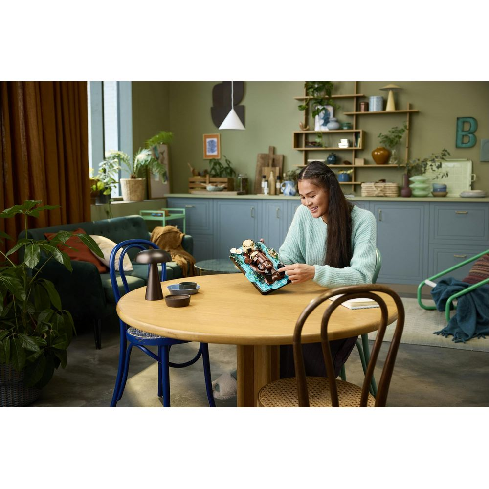 Kobieta siedzi przy okrągłym drewnianym stole i patrzy na kolorowy model.