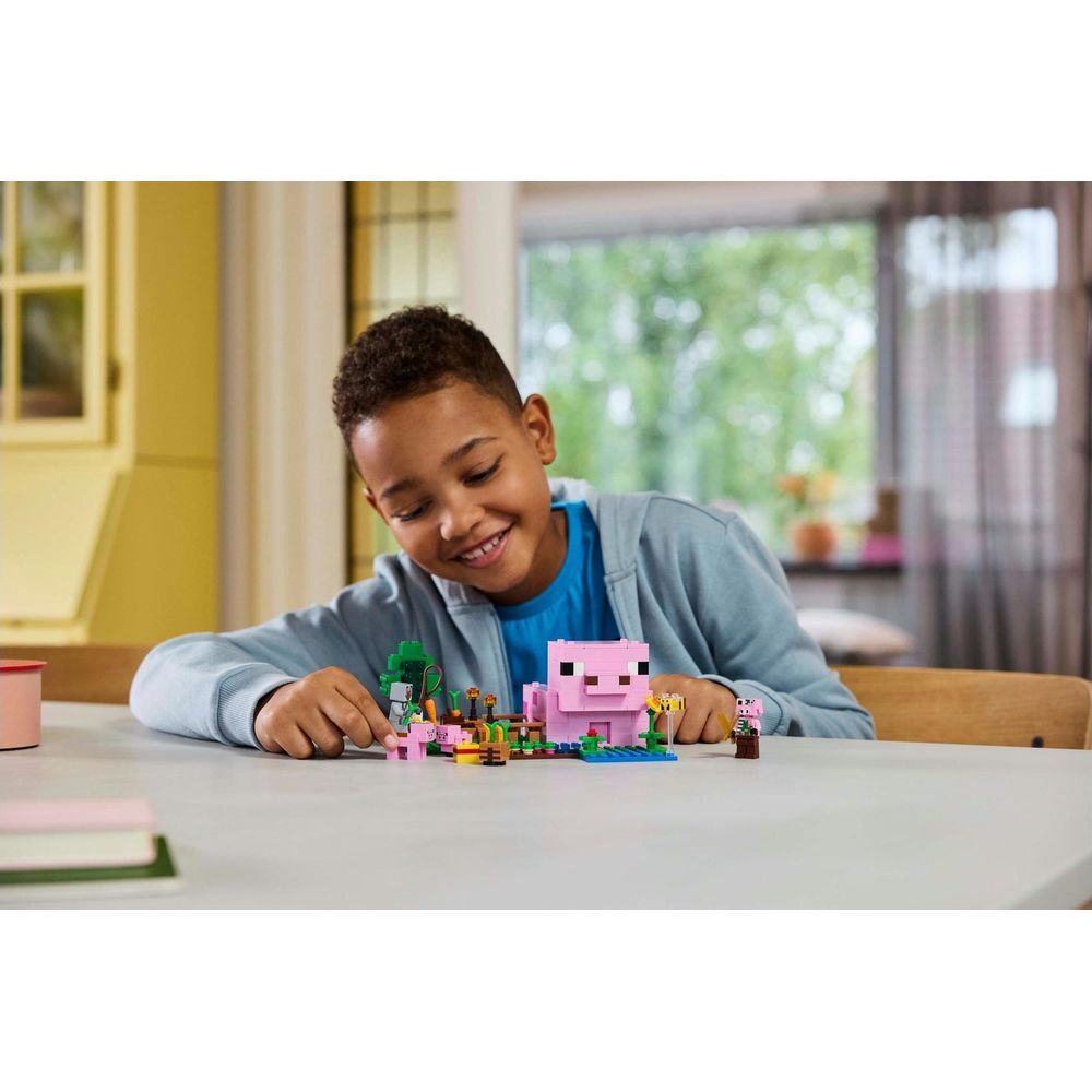 Chłopiec bawi się figurkami LEGO Minecraft przedstawiającymi różową świnię i drzewo.