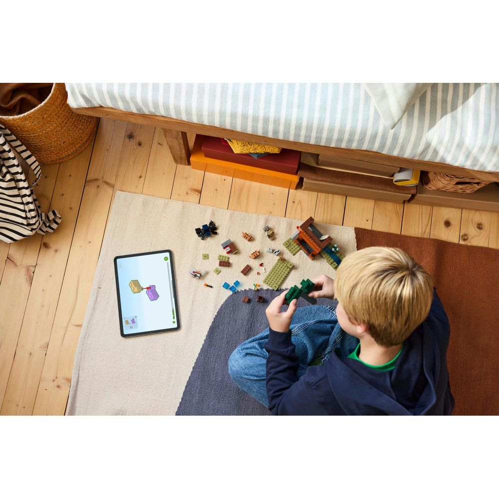 Dziecko buduje z kolorowych klocków Lego na dywanie. Tablet pokazuje instrukcje budowania.