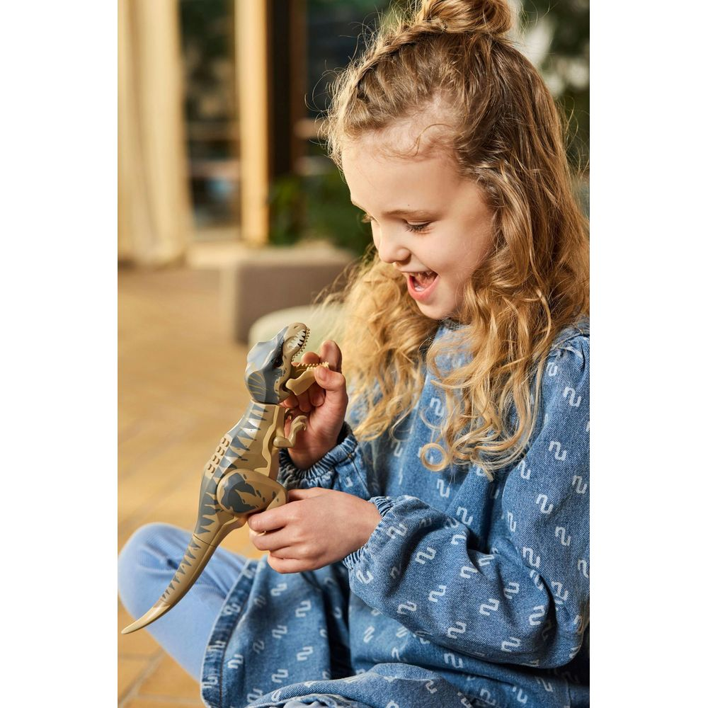 Mała dziewczynka w niebieskiej sukience dżinsowej bawi się zabawką dinozaura.