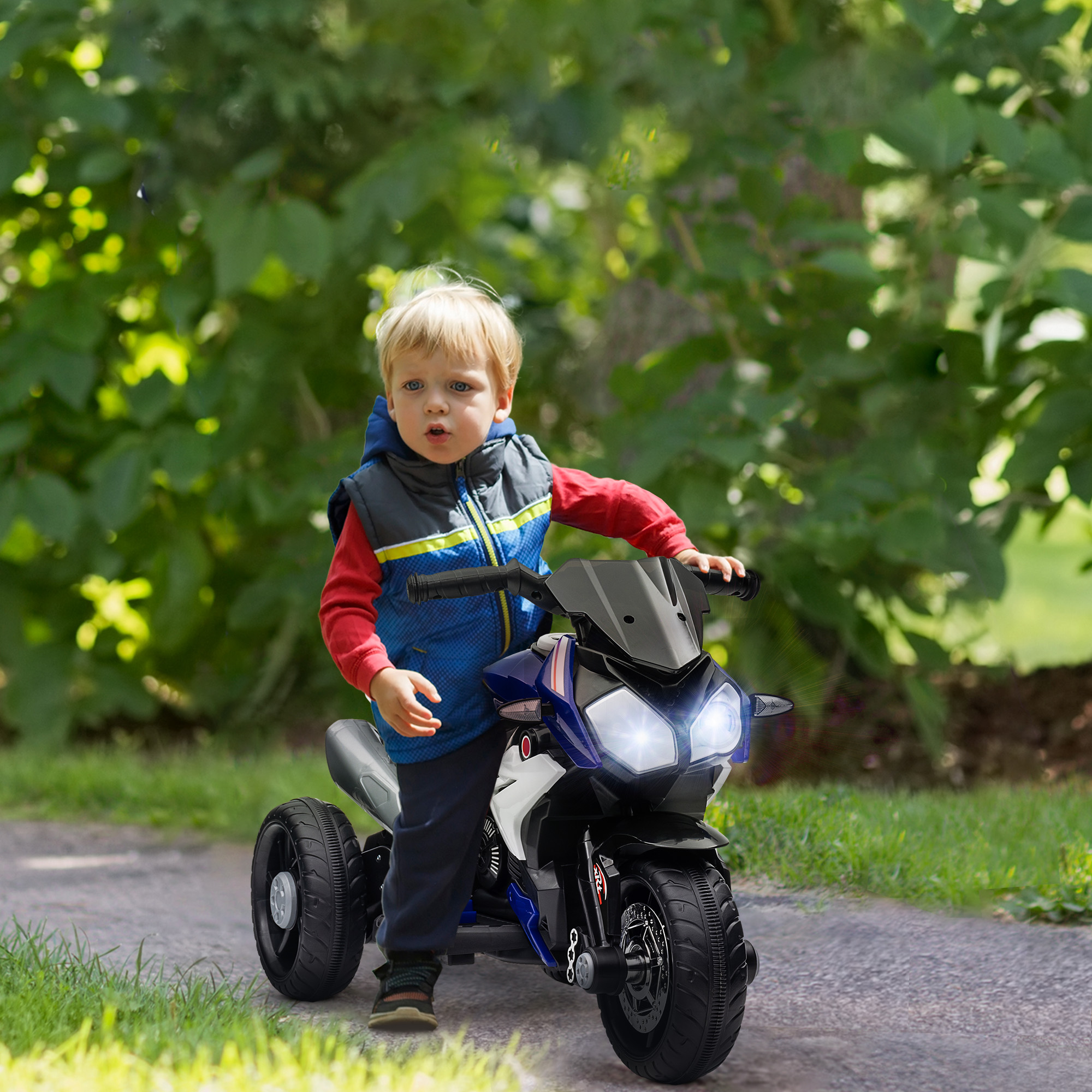 Un niño pequeño de pelo rubio se sienta en una moto de juguete azul al aire libre.