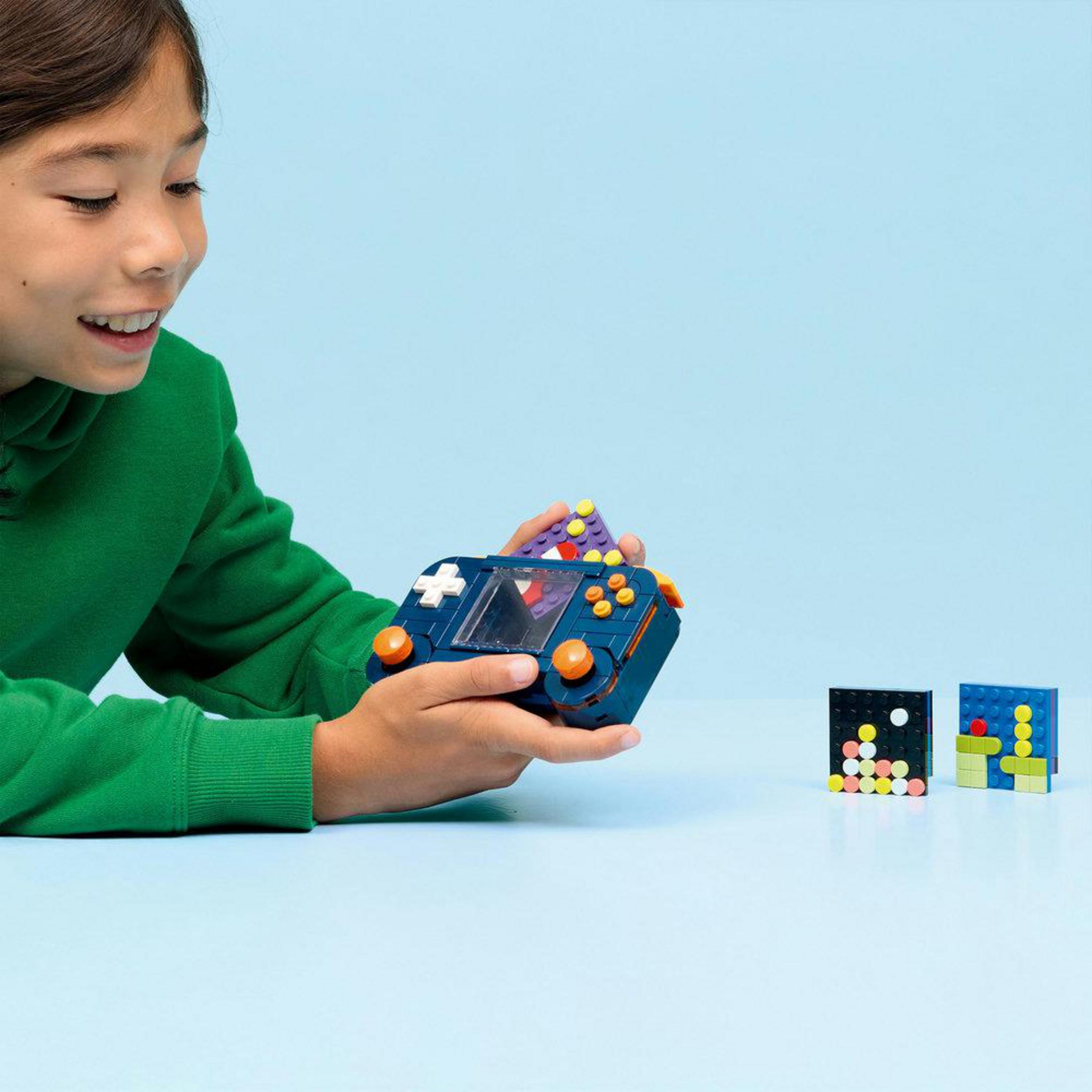 Dziecko bawi się niebieską grą Lego i dwoma kolorowymi klockami.