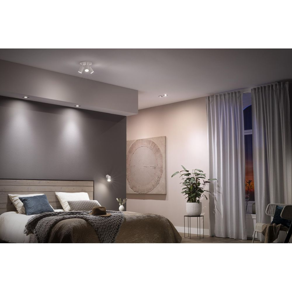 Een slaapkamer met bed, gordijnen en een raam bij schemering.