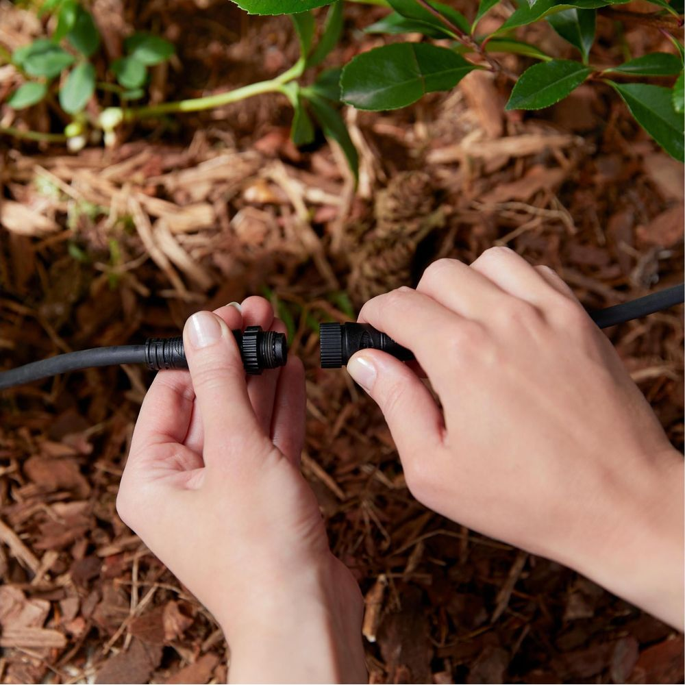 Hände verbinden ein schwarzes Kabel mit einem Stecker über Rindenmulch.