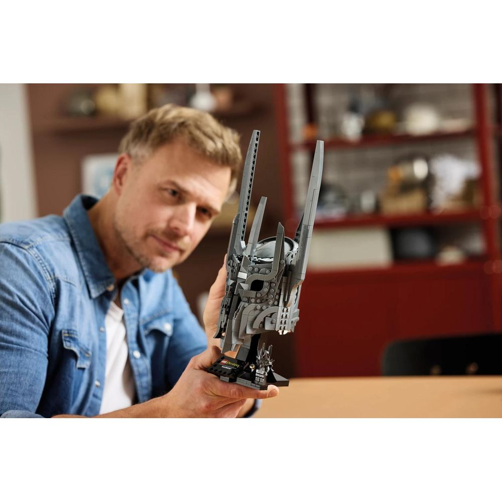 Mężczyzna w dżinsowej koszuli trzyma szary model hełmu Lego. Rozmyte tło.