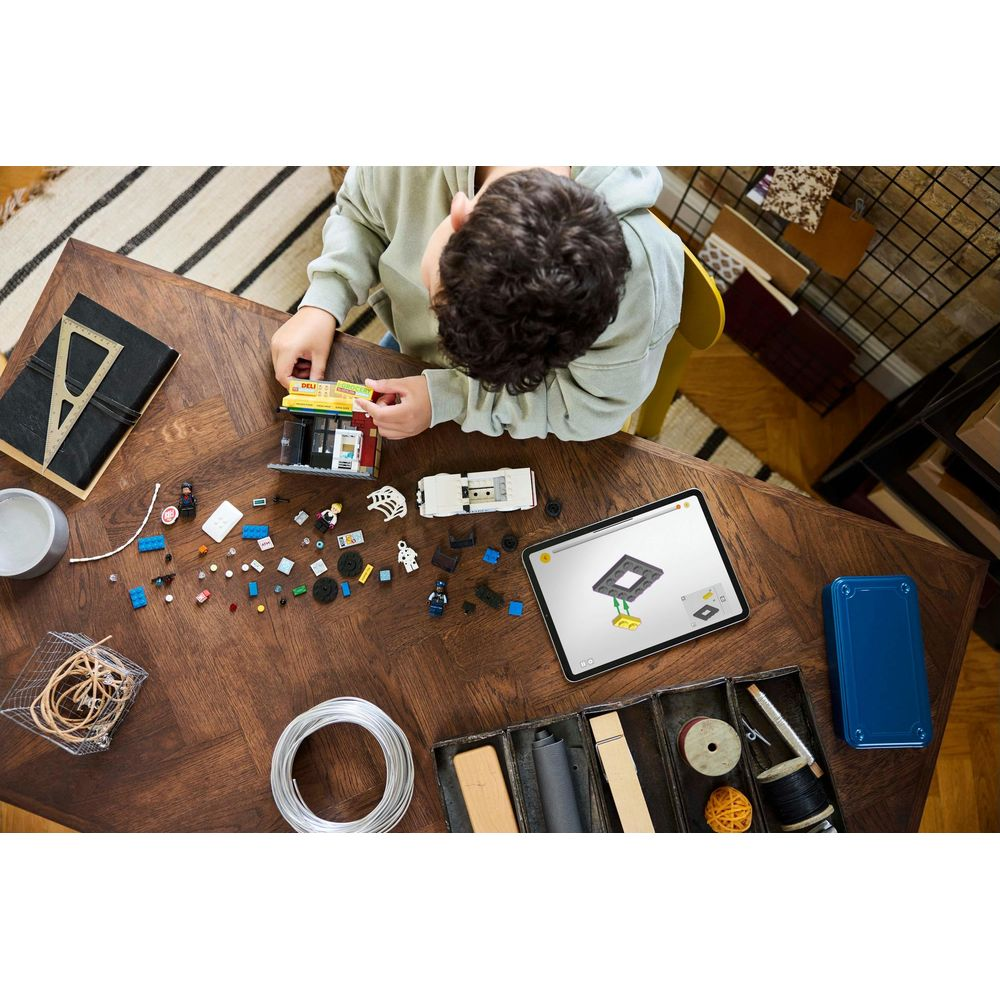 Dziecko buduje model Lego z instrukcjami na tablecie. Części i samochód na stole.