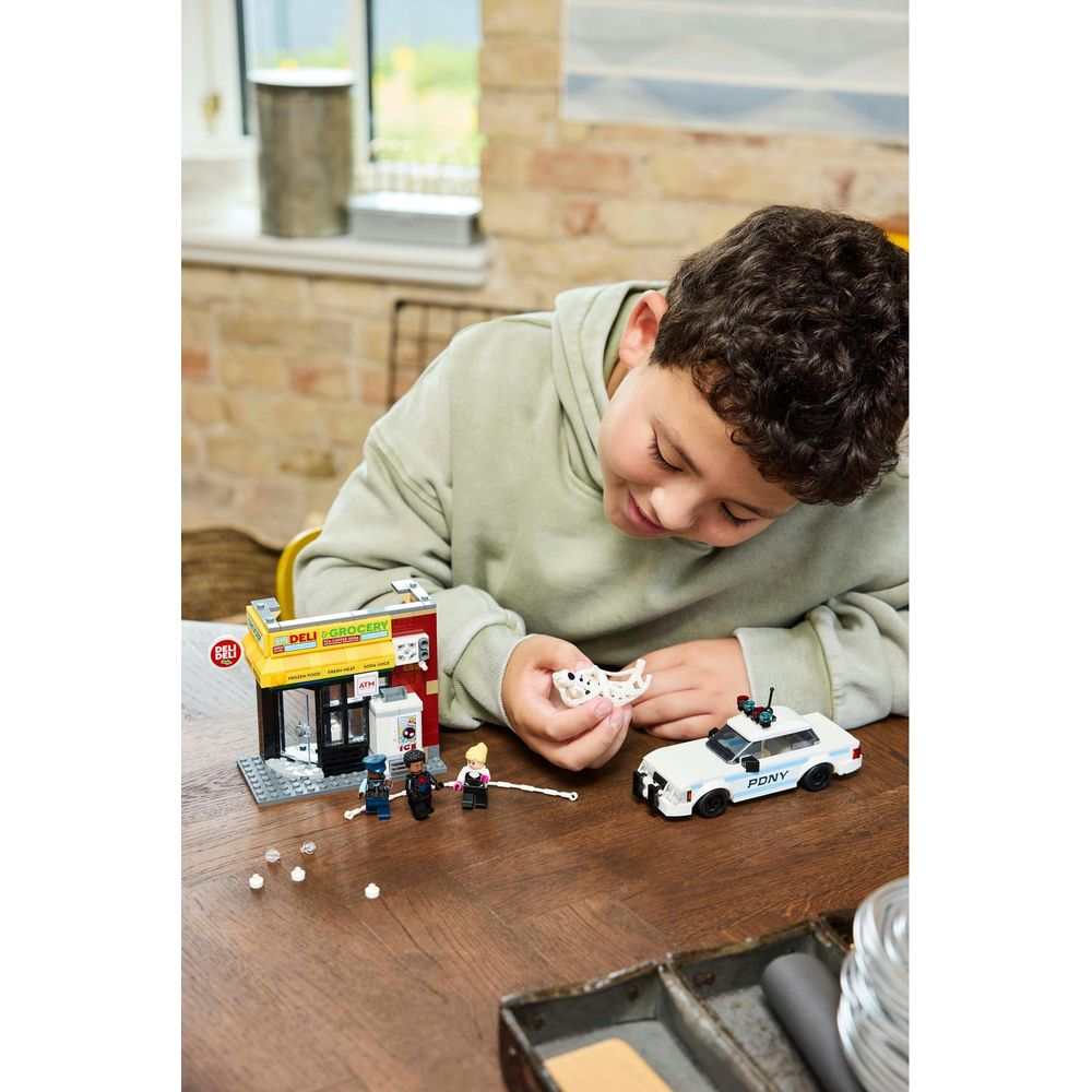 Chłopiec bawi się figurkami LEGO, sklepem i radiowozem przy drewnianym stole.