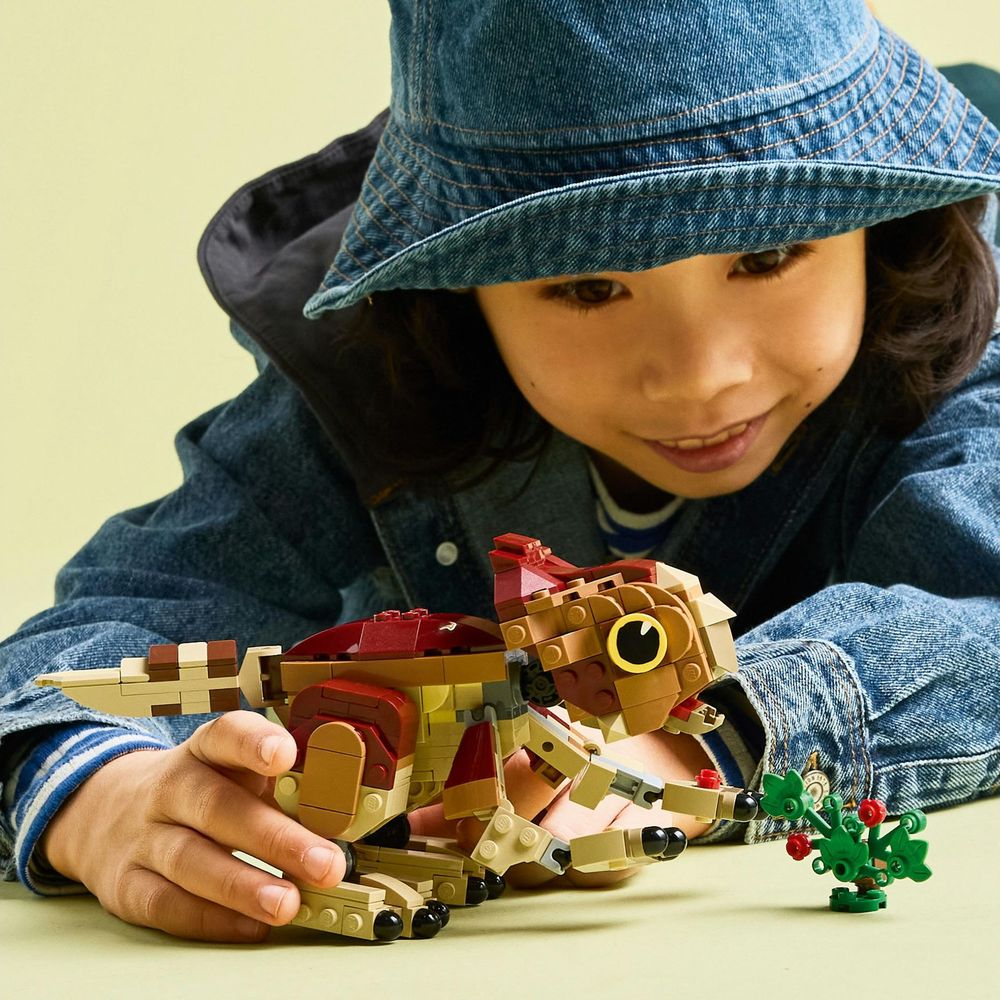 Dziecko w dżinsowym kapeluszu i kurtce bawi się dinozaurem Lego i małą rośliną.