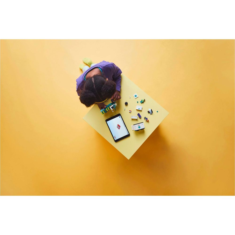 Dziecko buduje z kolorowych klocków Lego i tabletu na żółtym stole.