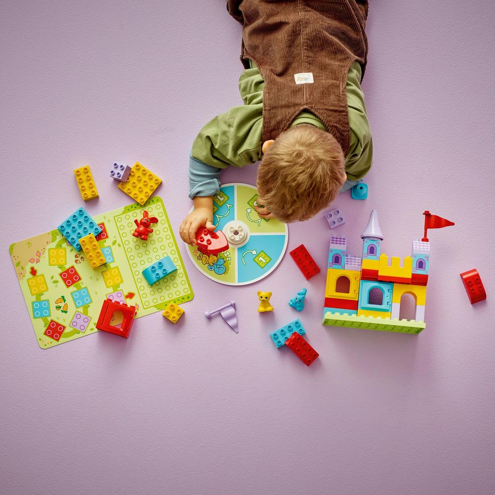 Dziecko bawi się kolorowymi klockami Lego i planszą na fioletowym tle.