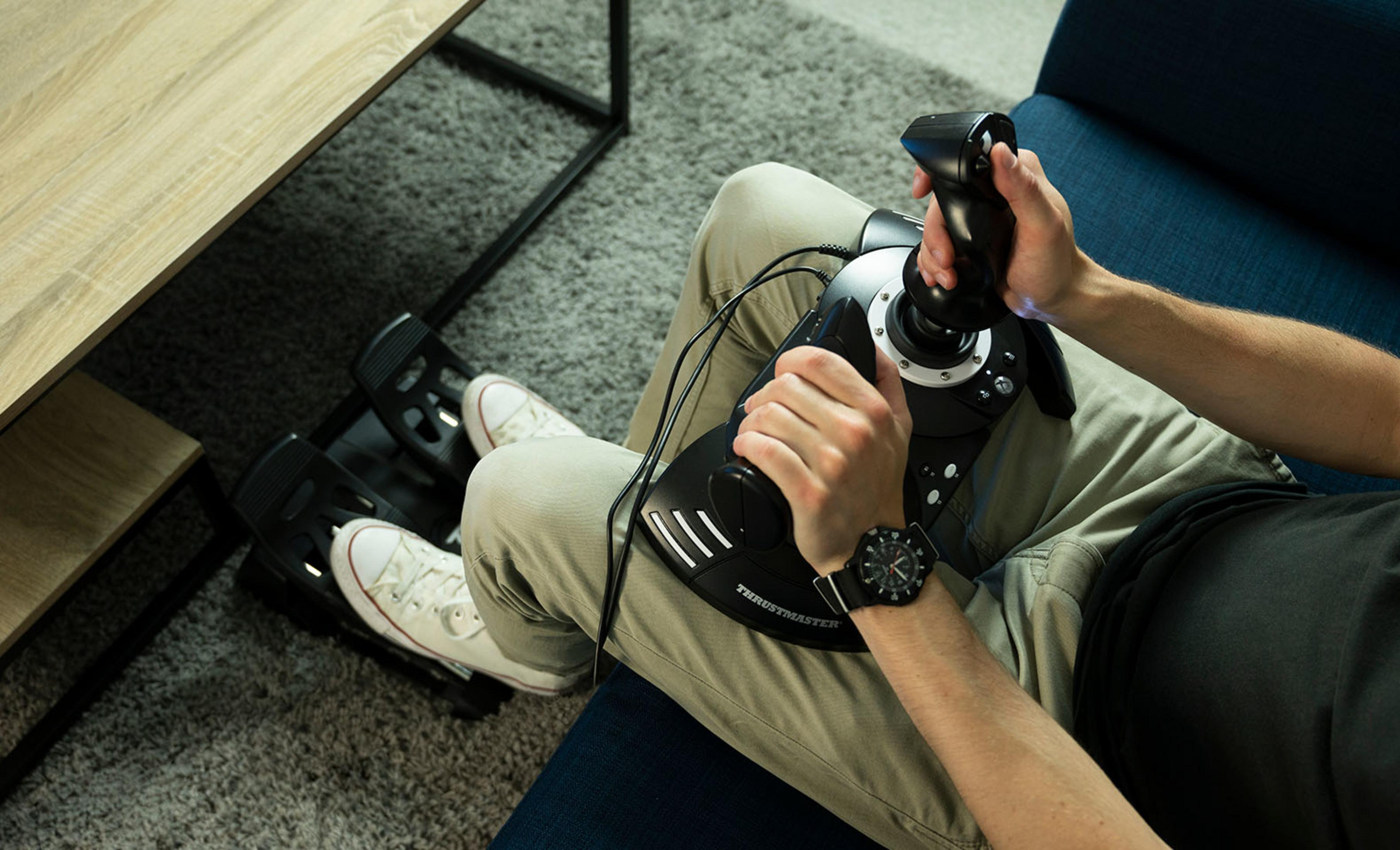 Osoba z joystickiem i pedałami na dywanie gra w symulator lotu.