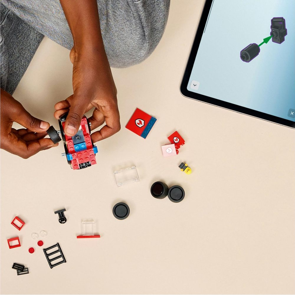 Osoba buduje czerwony samochód Lego z tabletem jako instrukcją.