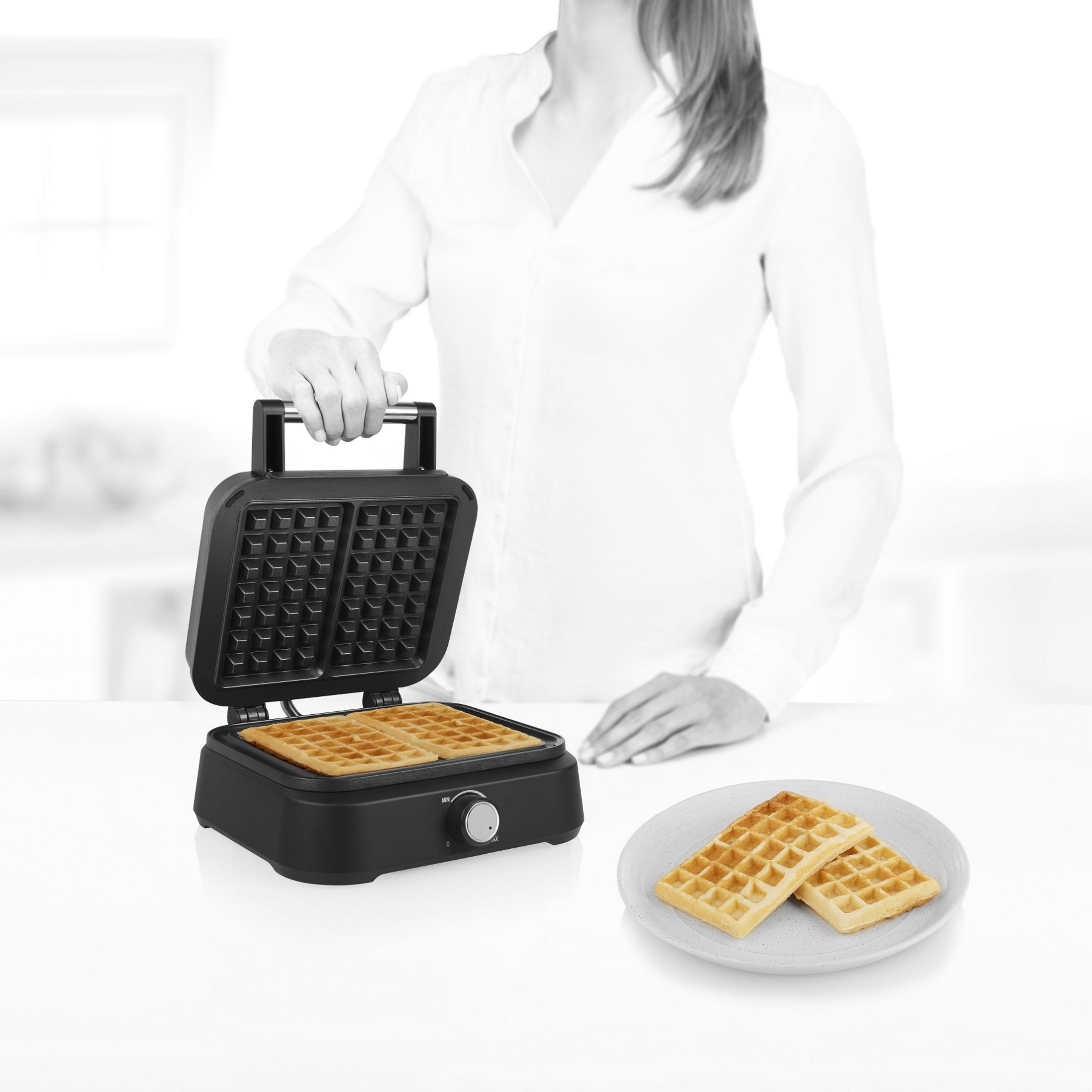 Osoba otwiera gofrownicę z czterema goframi w środku i dwoma na talerzu.