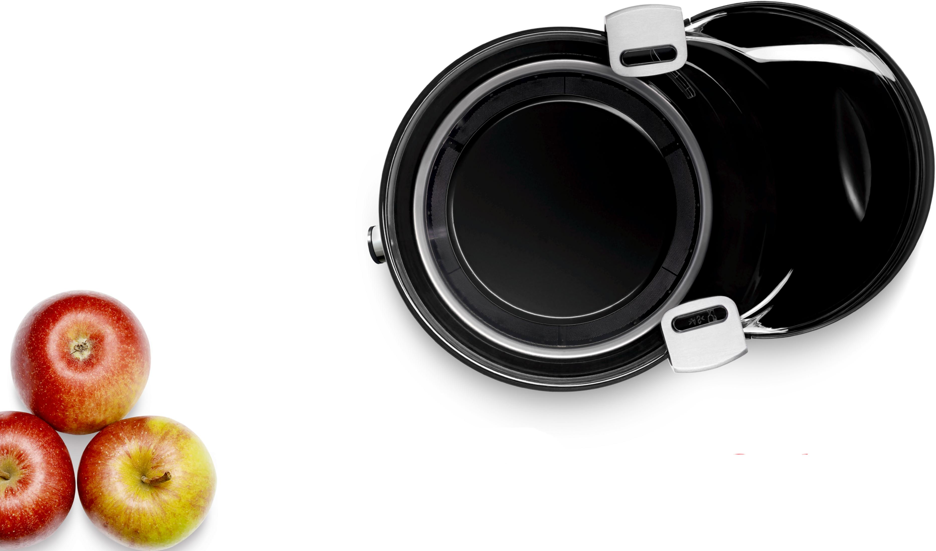 Trois pommes à gauche d'une marmite noire ouverte avec poignées argentées.