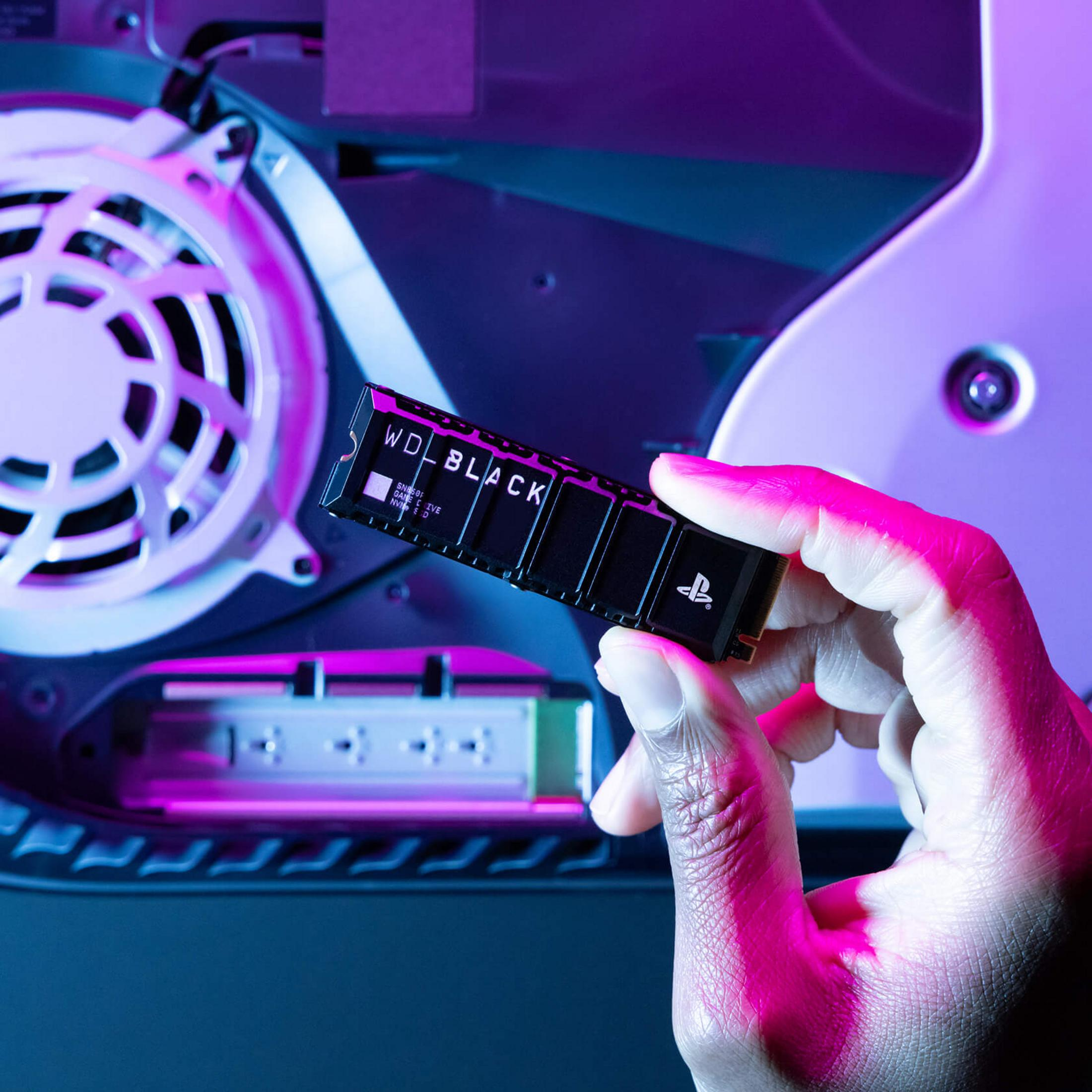 Ręka trzyma dysk SSD WD Black obok wentylatora i elektroniki.