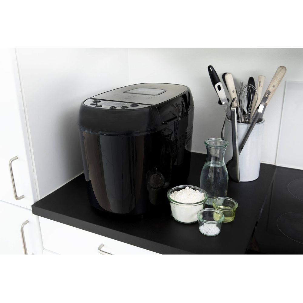 Czarna maszyna do wypieku chleba z składnikami i przyborami.