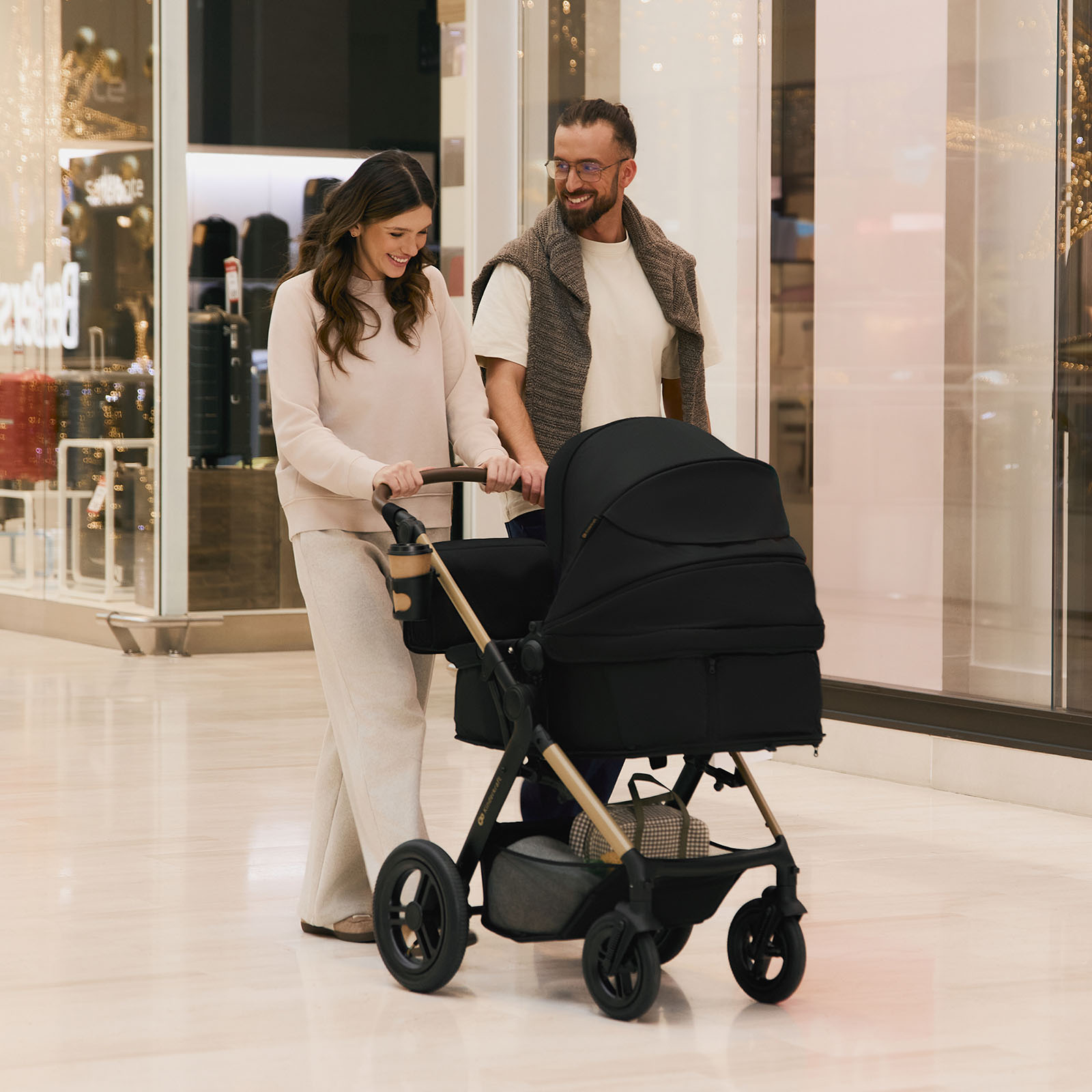 Ein Paar schiebt einen schwarzen Kinderwagen in einem Einkaufszentrum.