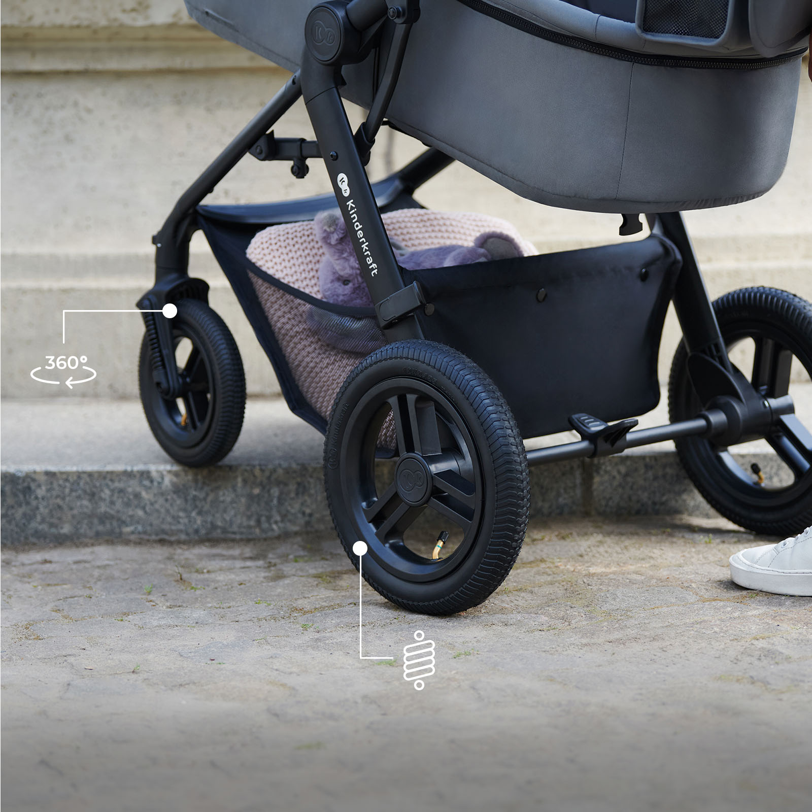 Ein Kinderwagen mit grauer Sitzeinheit und schwarzen Rädern steht auf Stufen.
