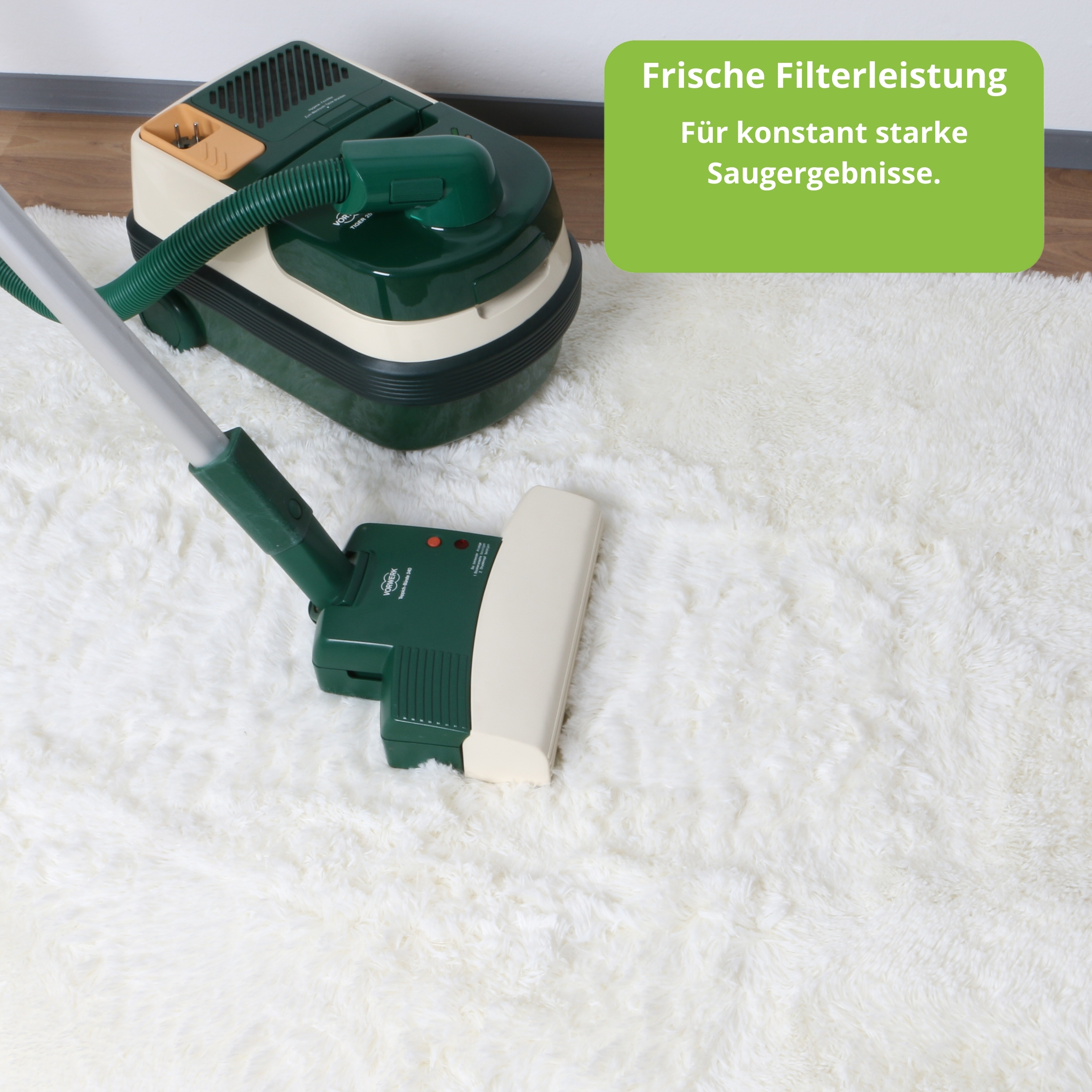 Ein grüner und cremefarbener Staubsauger mit Bürste auf weißem Teppich.