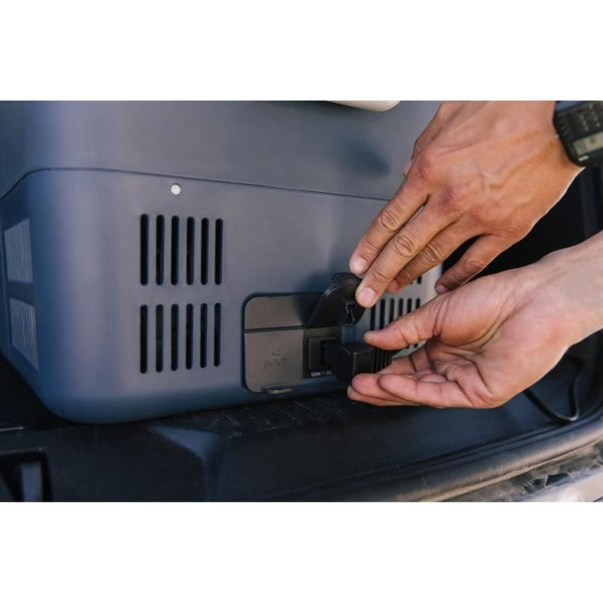 Ręce wpinające kabel do niebieskiego pudełka z otworami wentylacyjnymi.