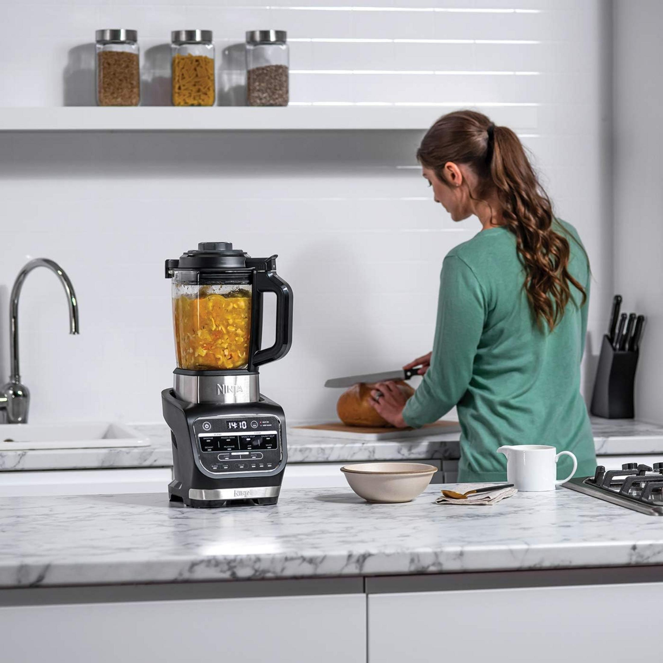 Kobieta kroi chleb w kuchni obok blendera z zupą.