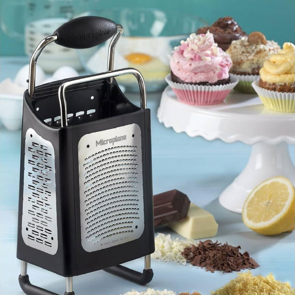 Kulp ve tutamaklı siyah bir Microplane rendesi, etrafında kekler, çikolata ve limon.