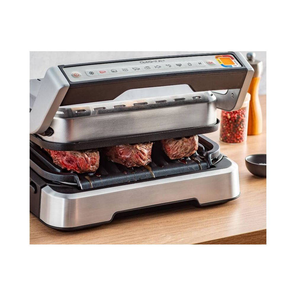 Trzy steki gotujące się na srebrnym grillu kontaktowym z panelem sterowania.