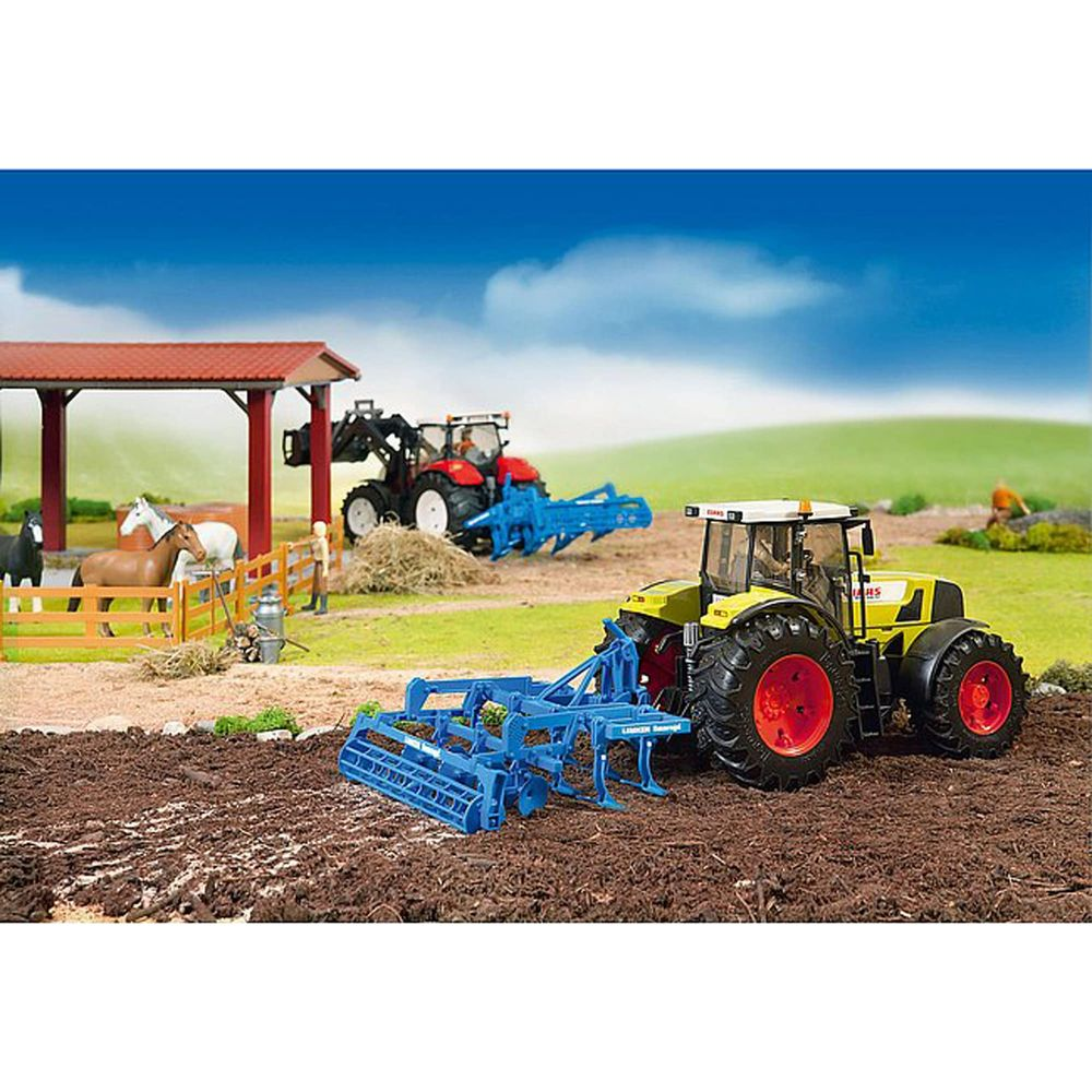 Un trattore giallo con erpice blu è in un campo. Un trattore rosso sullo sfondo.