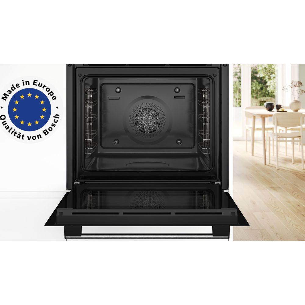 Otwarty piekarnik Bosch z pieczęcią "Wyprodukowano w Europie" i stołem w jadalni w tle.