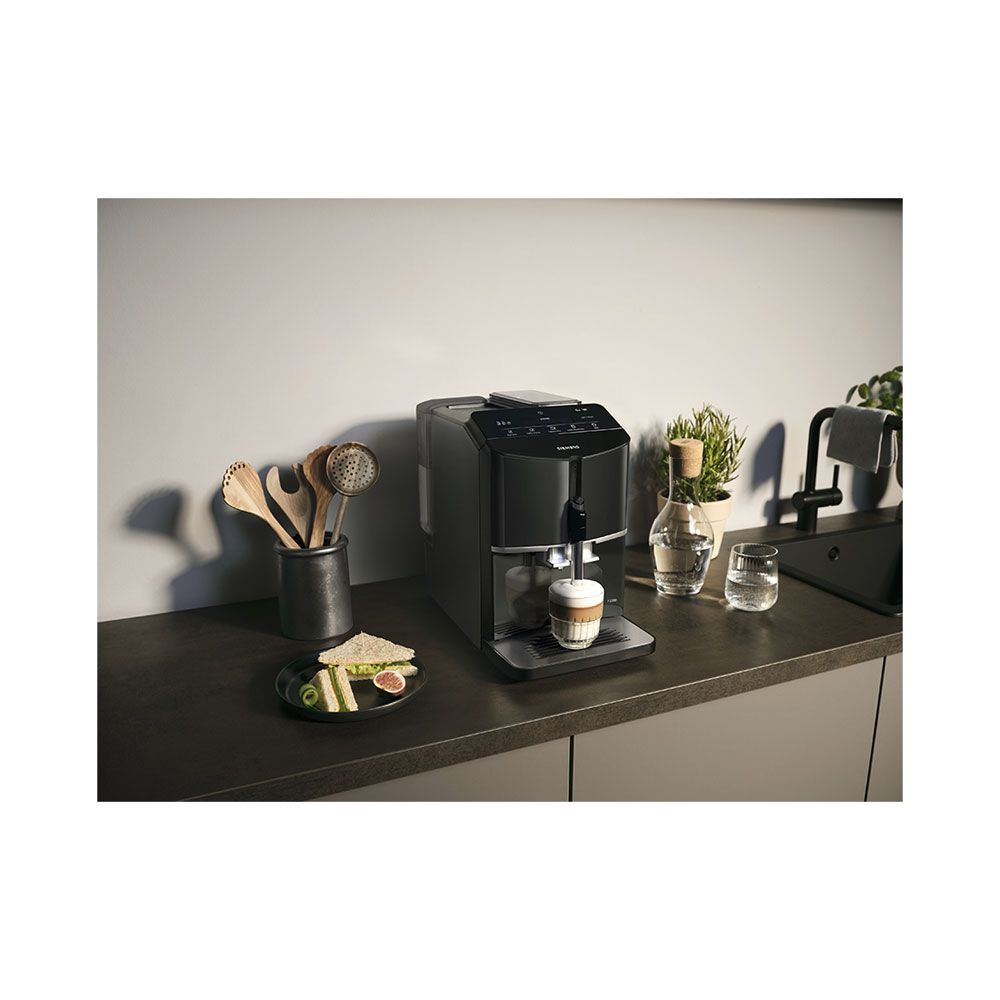 Une machine à café noire prépare un cappuccino, avec un sandwich et des verres à proximité.