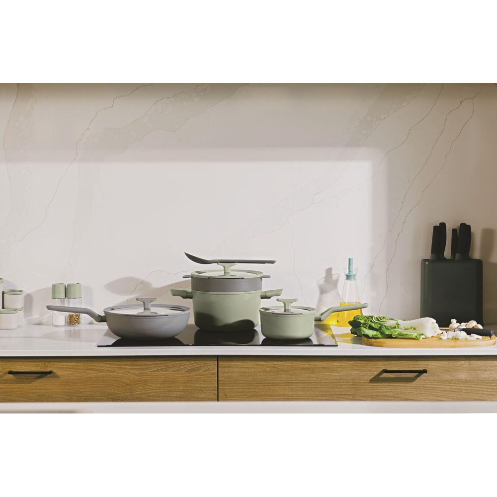 Green and grey cookware on an induction hob with vegetables.