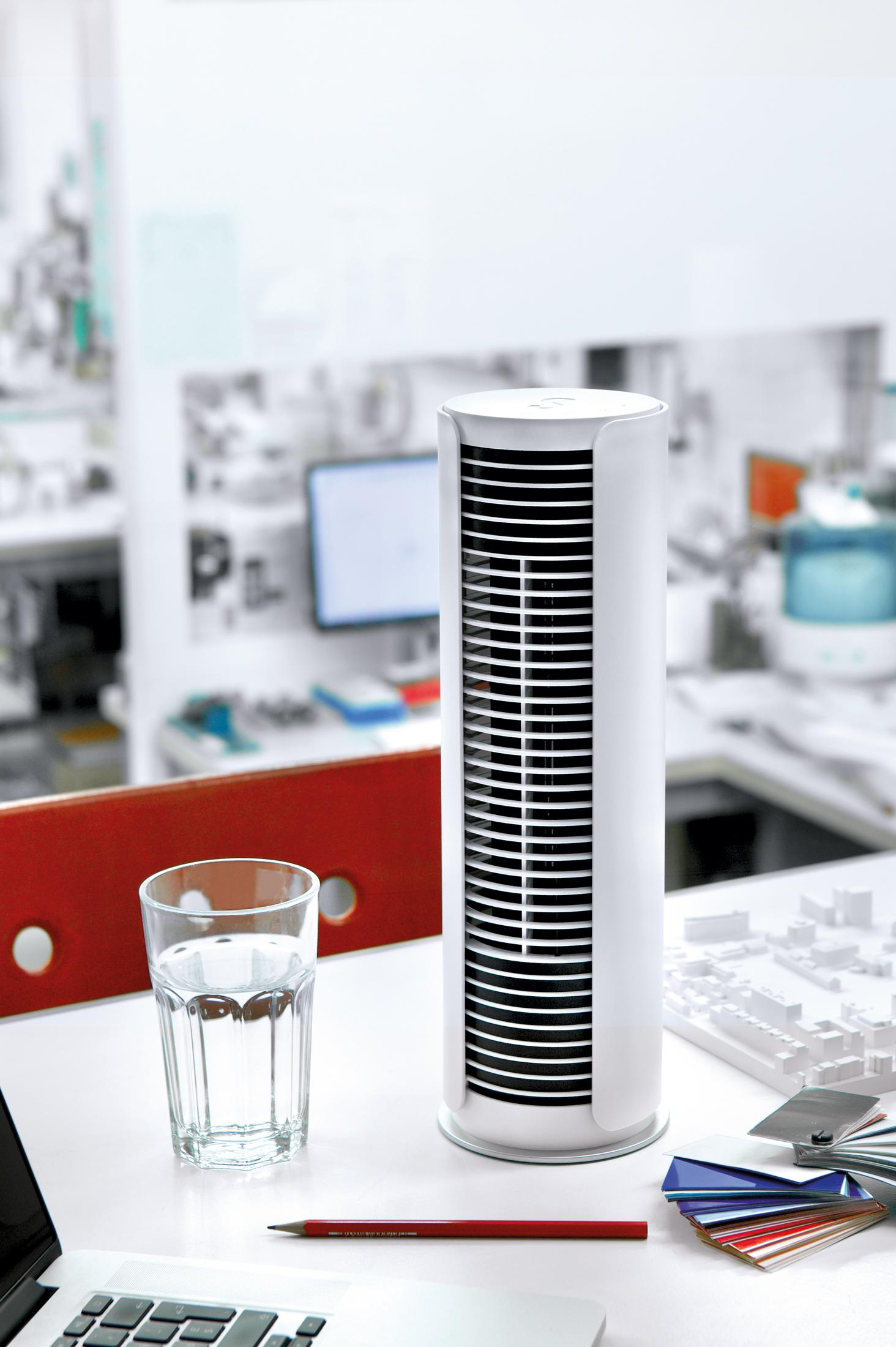 Un ventilateur tour sur un bureau à côté d'un verre d'eau.