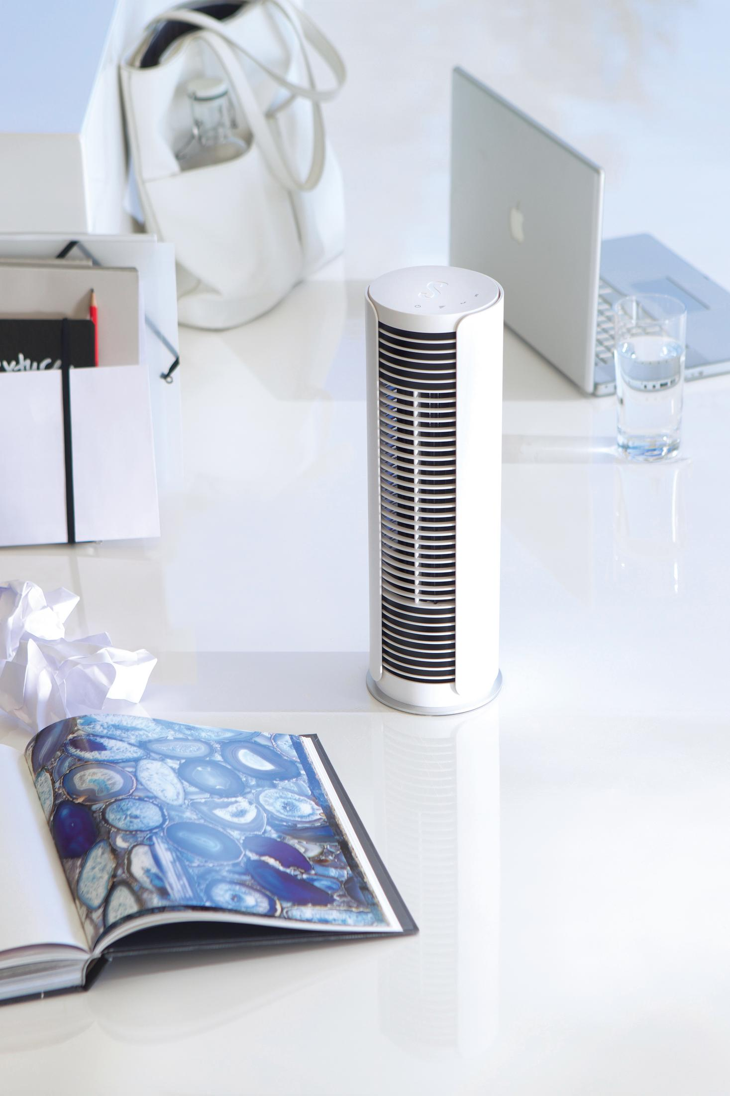 Un ventilateur tour blanc est sur un bureau à côté d'un ordinateur portable et d'un verre d'eau.