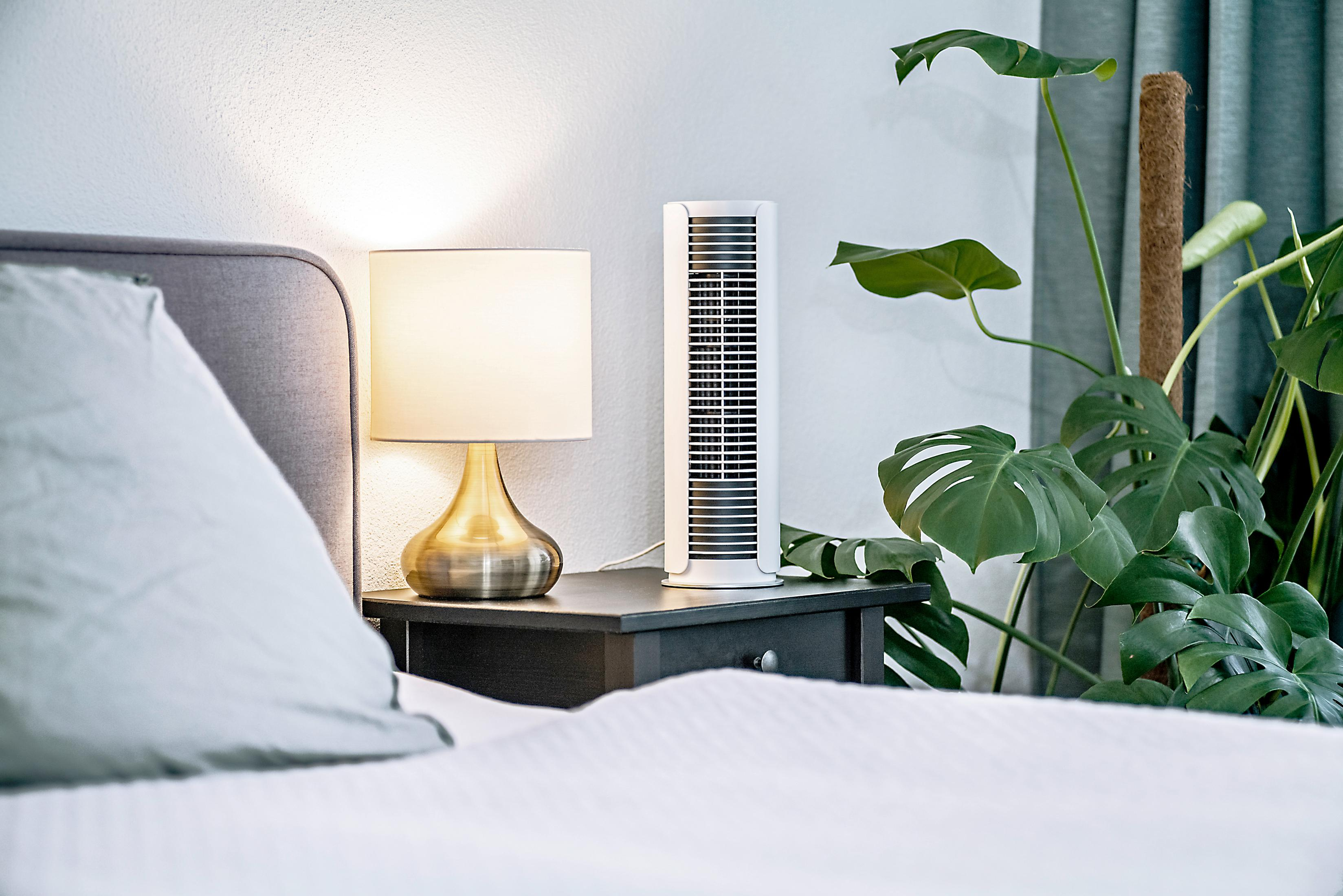 Une table de chevet avec lampe et ventilateur tour à côté d'un lit.