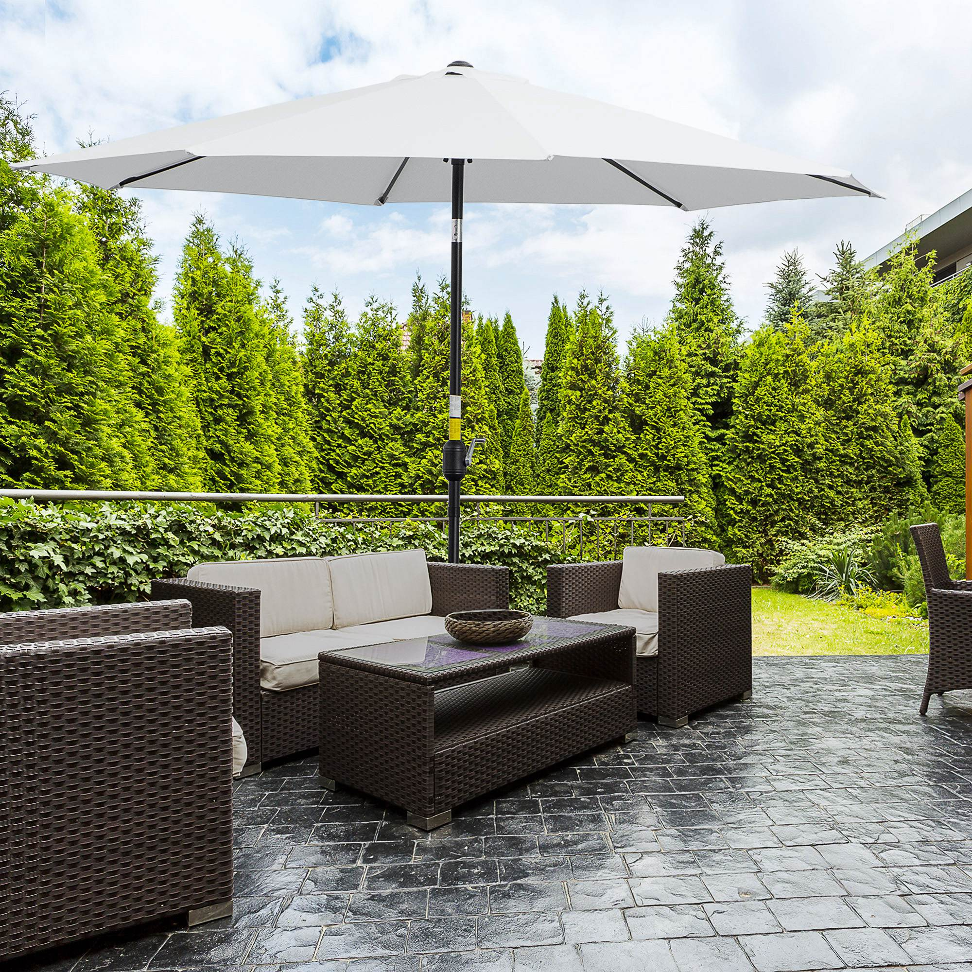 Set di mobili da esterno sotto ombrellone bianco su patio pavimentato con alberi.