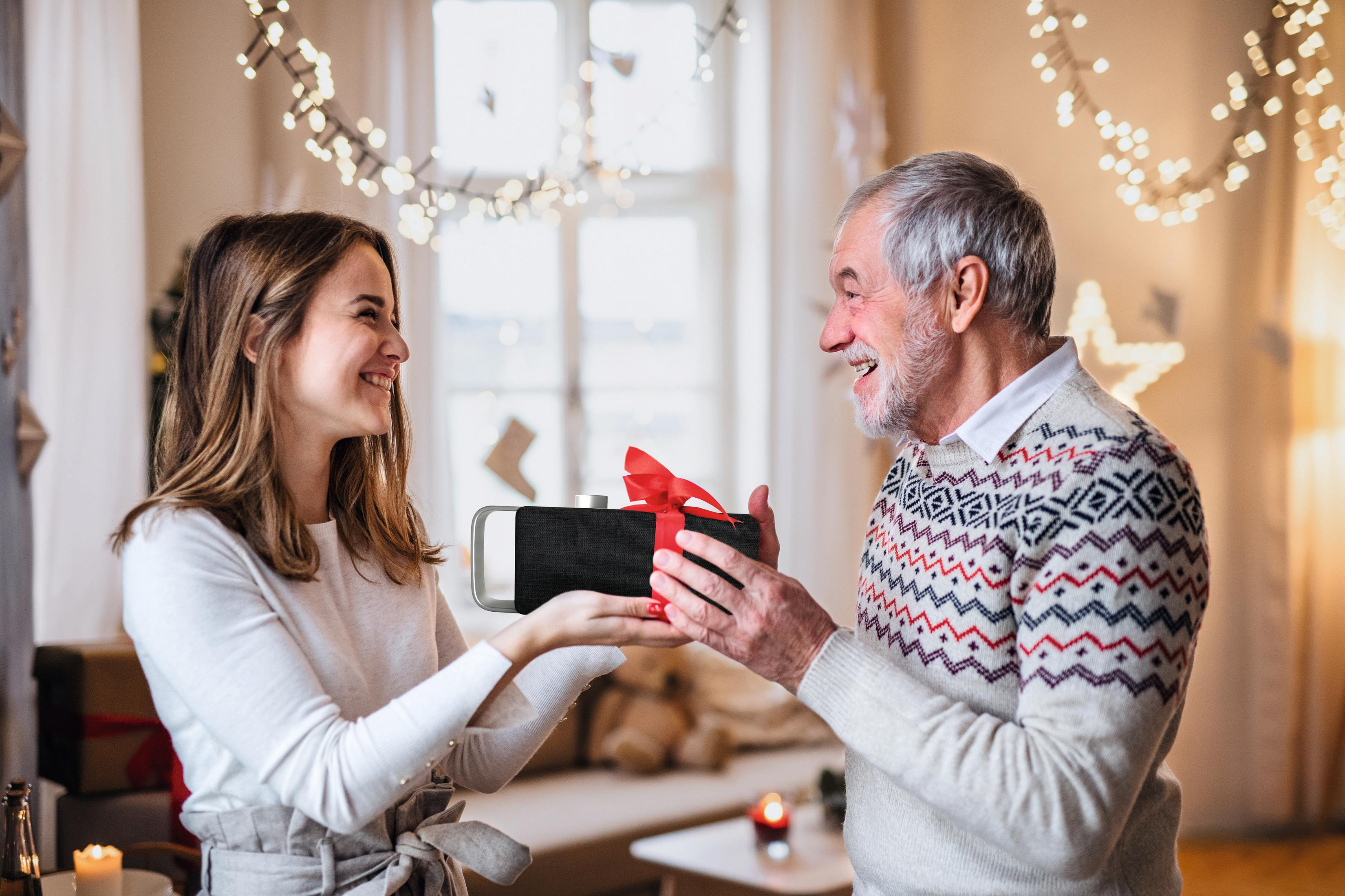 Man en vrouw wisselen een cadeau uit, verlicht door slingers.