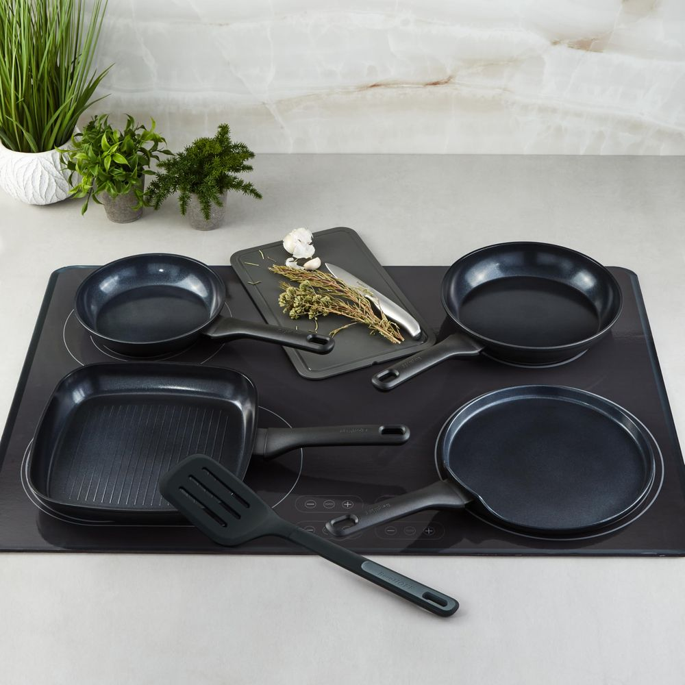 Ensemble d'ustensiles de cuisine sur plaque à induction avec herbes et ail.