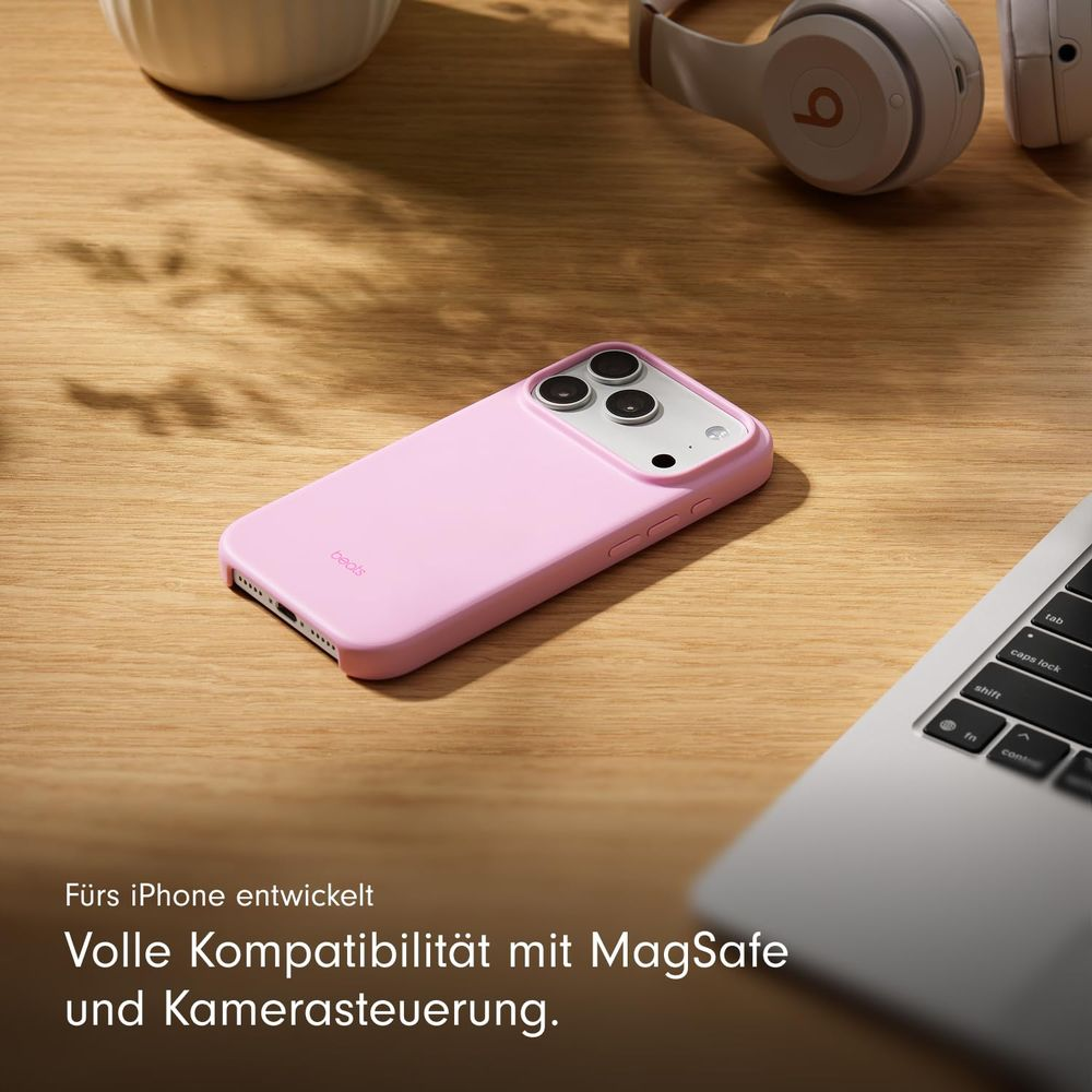 Różowe etui na iPhone leży na drewnianym stole obok słuchawek i laptopa.