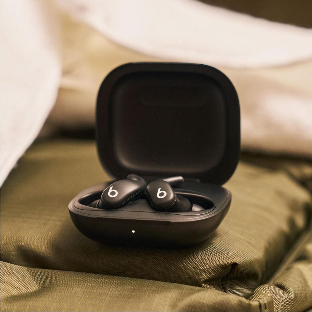 Czarne słuchawki Beats w otwartym etui ładującym na oliwkowozielonej tkaninie.