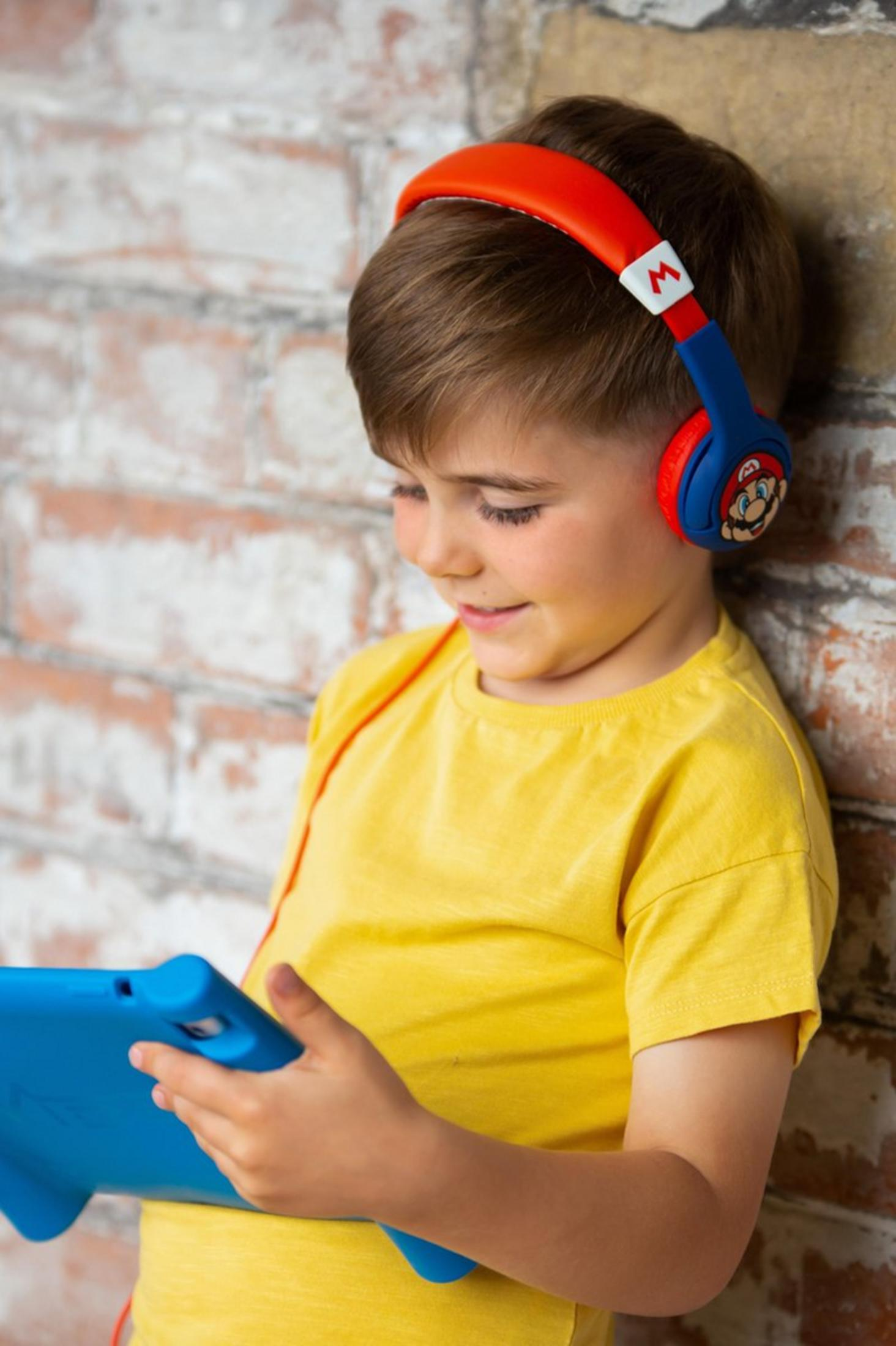 Chłopiec w słuchawkach z tabletem opiera się o ceglaną ścianę.