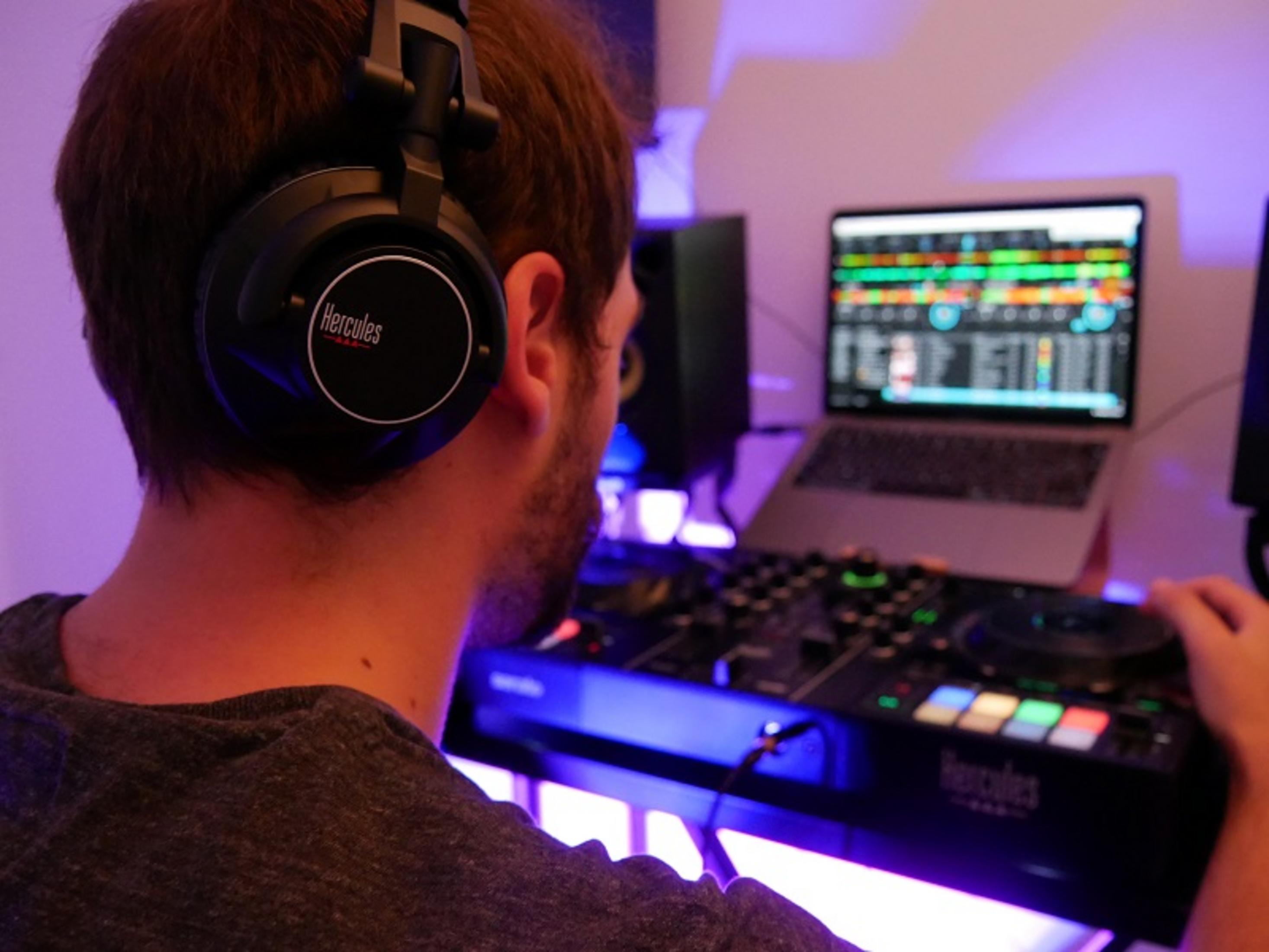 Mann mit Kopfhörern mischt Musik an einem DJ-Pult mit Laptop.