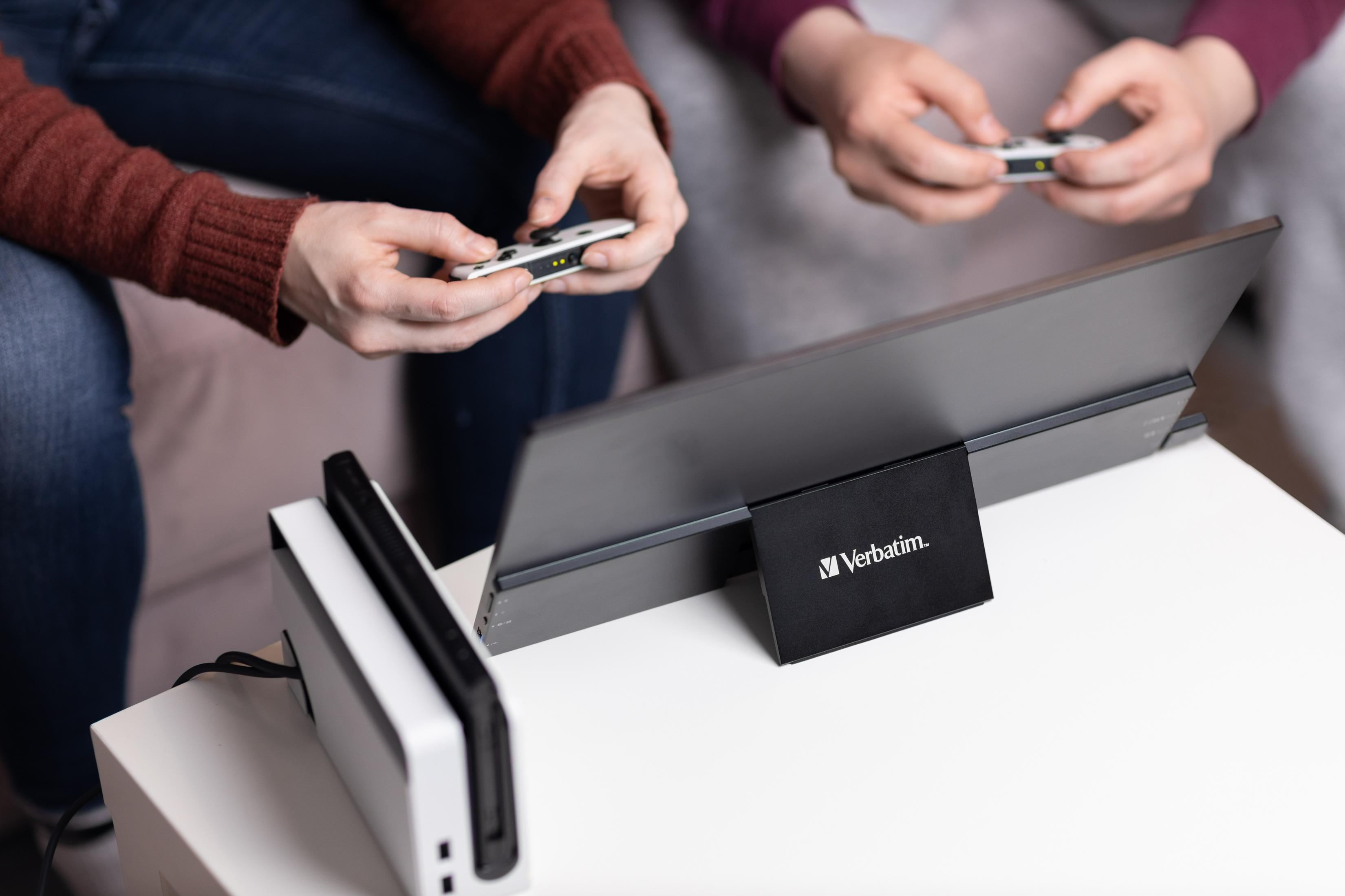 Dwie osoby grają w gry wideo za pomocą kontrolerów Joy-Con i przenośnego monitora.