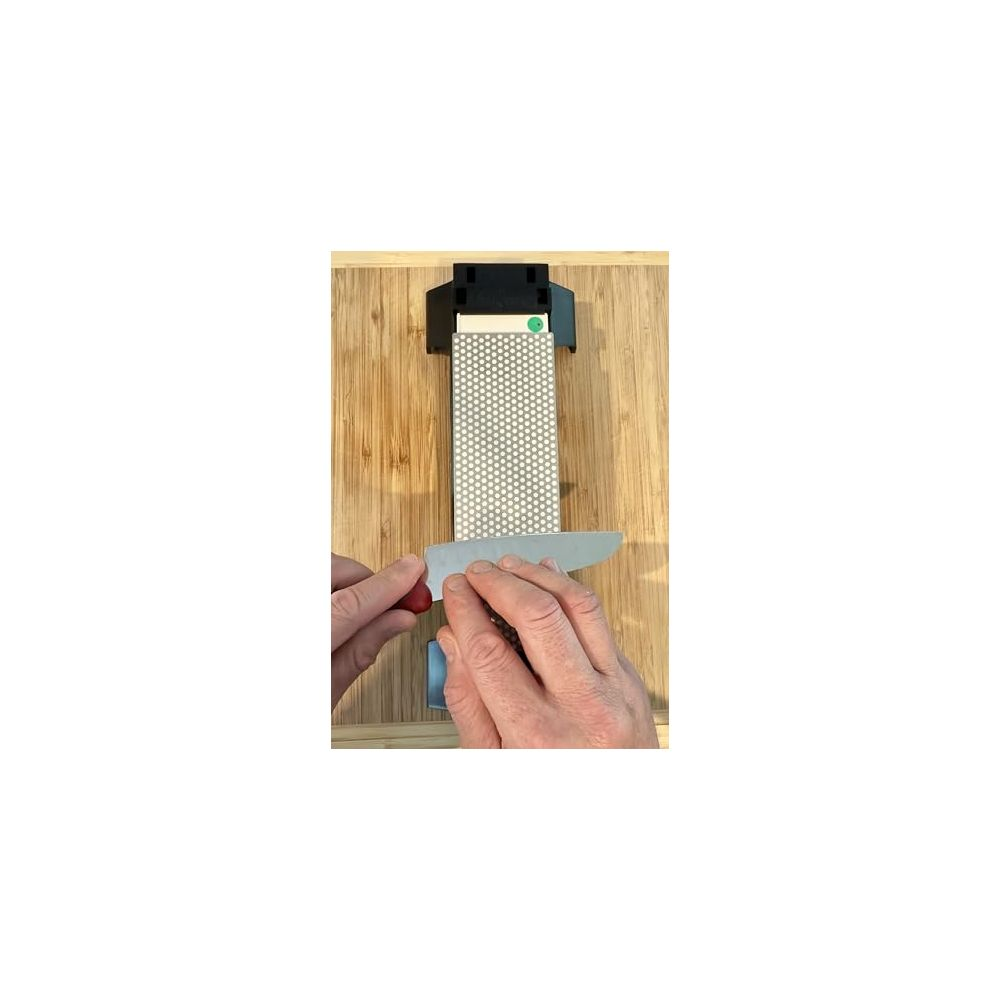 Mains affûtant un couteau sur une pierre diamantée posée sur une planche en bois.