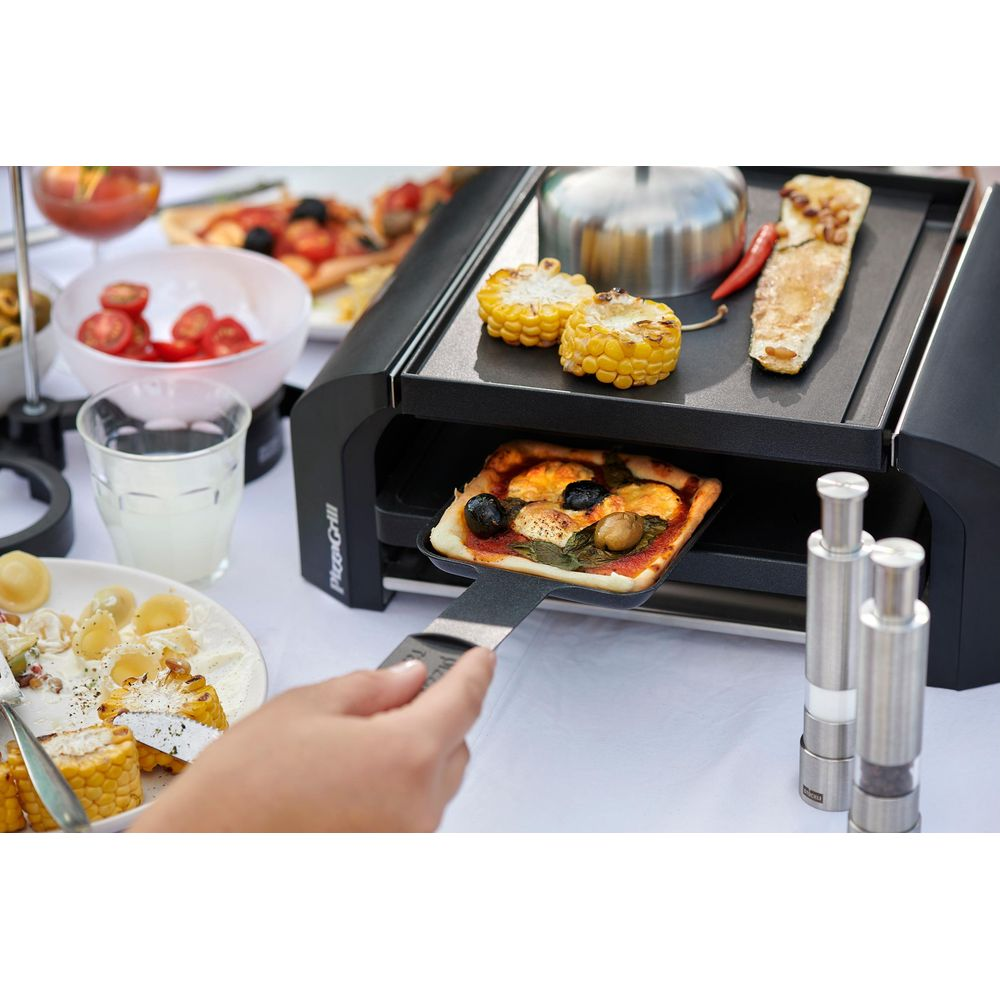 Une personne retire une petite pizza d'un grill. Des épis de maïs et des courgettes sont à proximité.